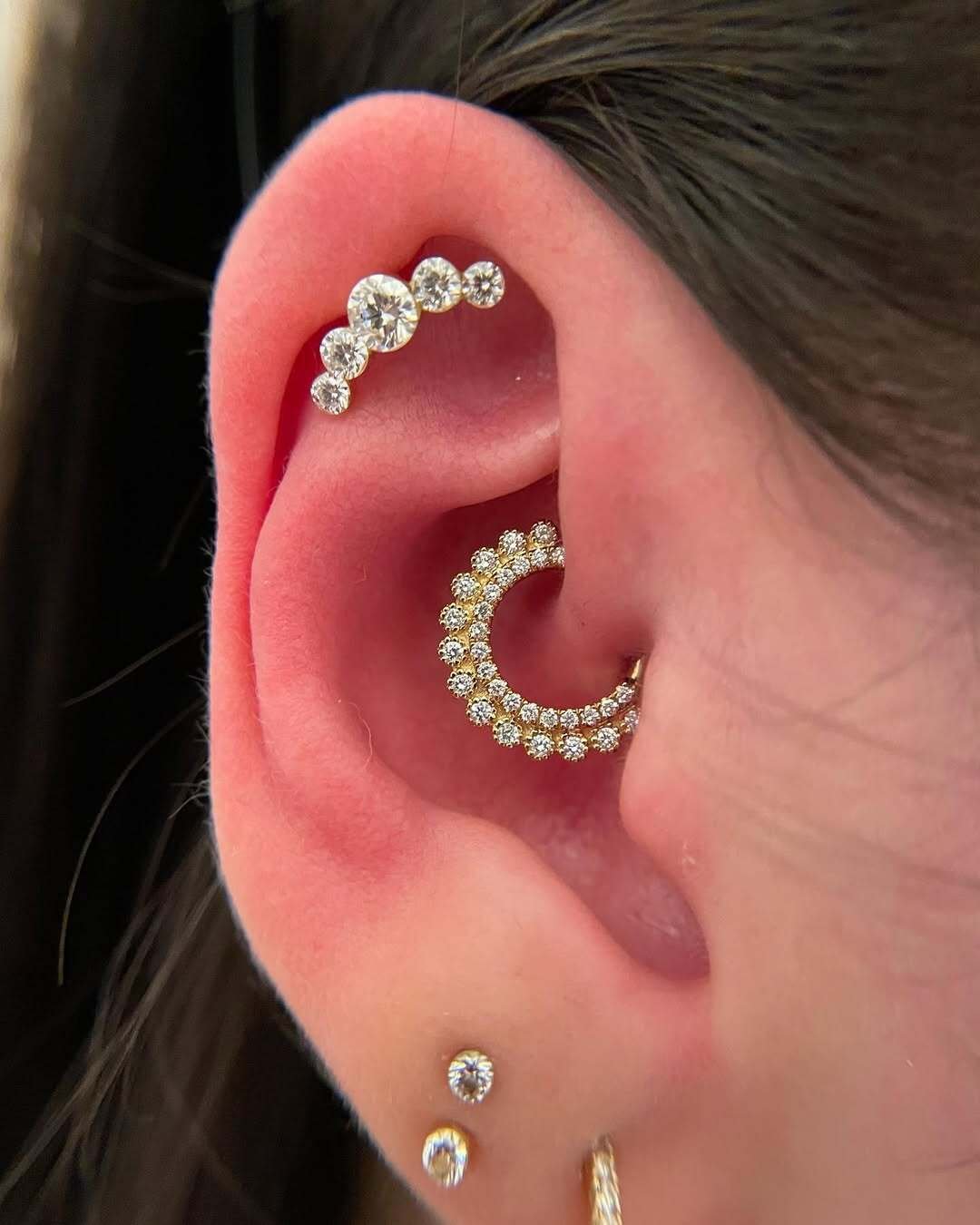 Close-up of an ear with multiple piercings featuring diamond-studded jewelry, including a curved helix and a conch earring.