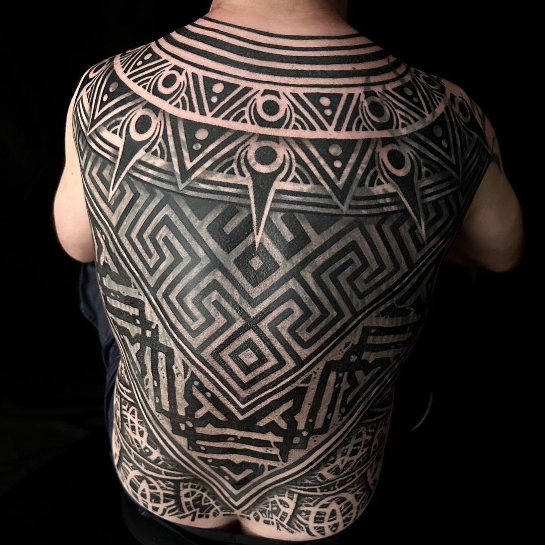 Intricate black geometric tattoo covering a person's back, featuring a maze-like design and tribal patterns.