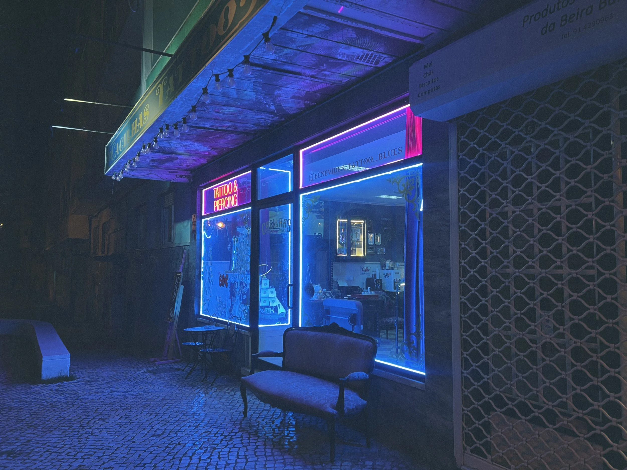 Cacilhas Tattoo Studio facade, Lisbon - blue neon on cobblestone street