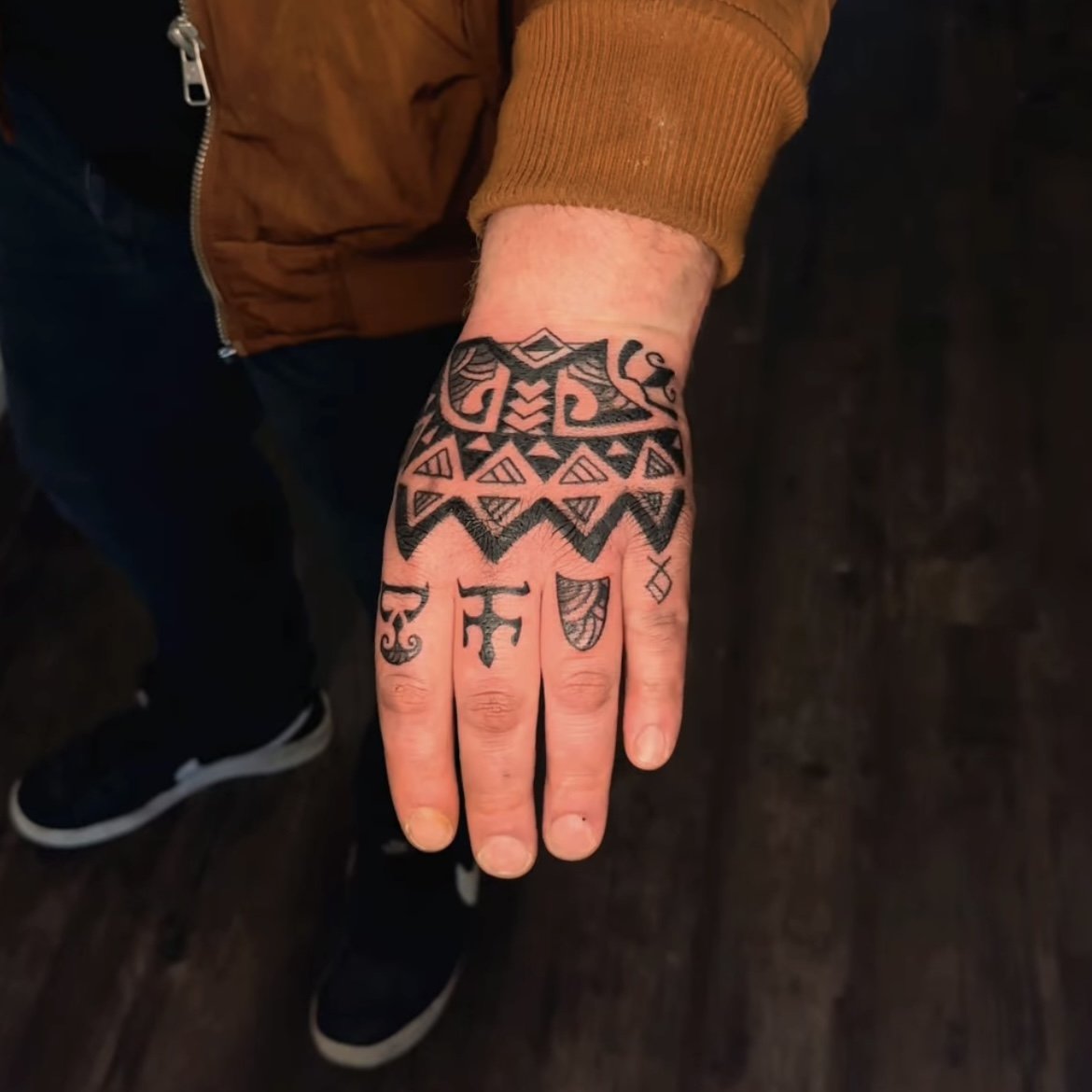Hand with intricate black geometric tattoos on fingers and back of the hand.
