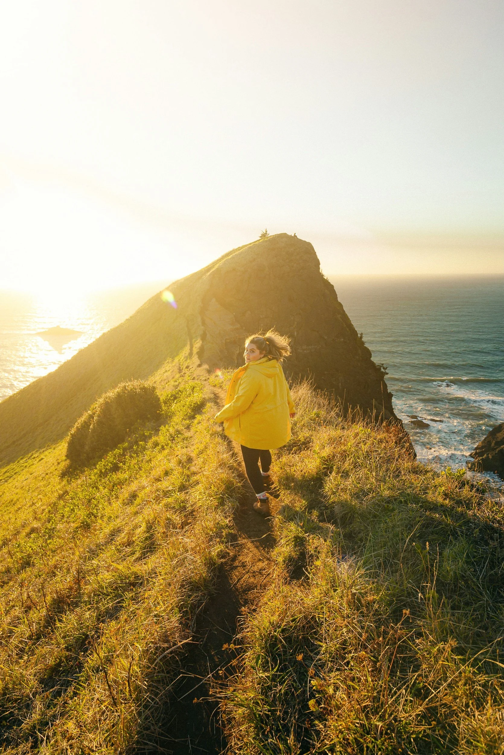 Woman in yellow jacket running along scenic outlook in the sun shining with ocean in the background