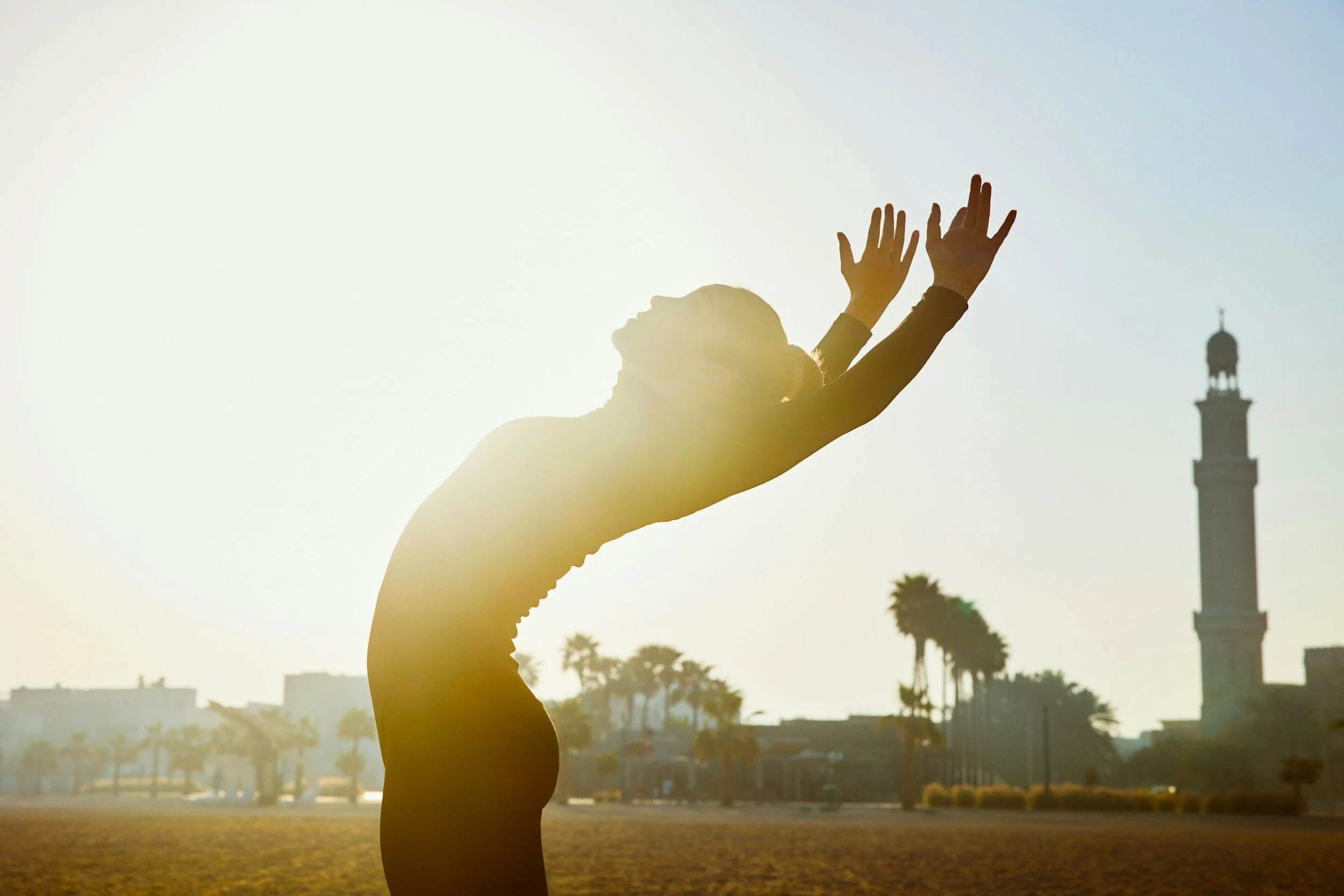 Sihloette of woman doing a graceful backbend dance with sun shining behind her