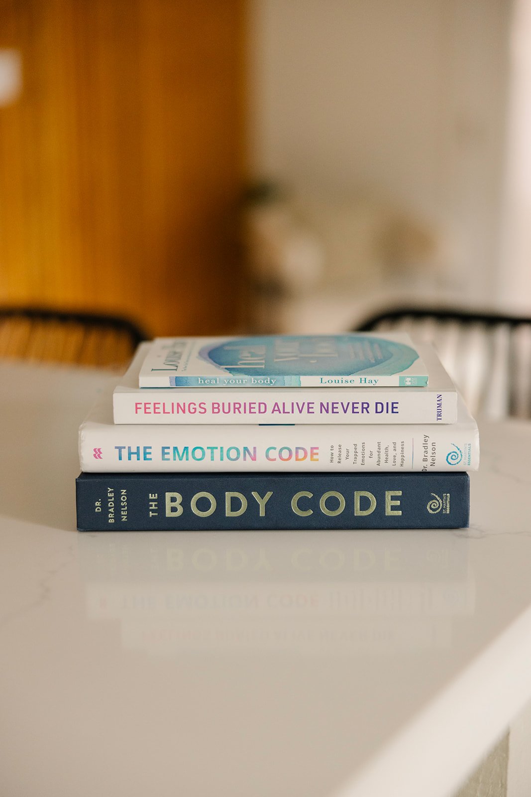 Stack of books on a table. Titles are The Body Code, The Emotion Code by Bradley Nelson, Feelings Buried Alive Never Die by Karol Truman and Heal Your Body by Louise Hay