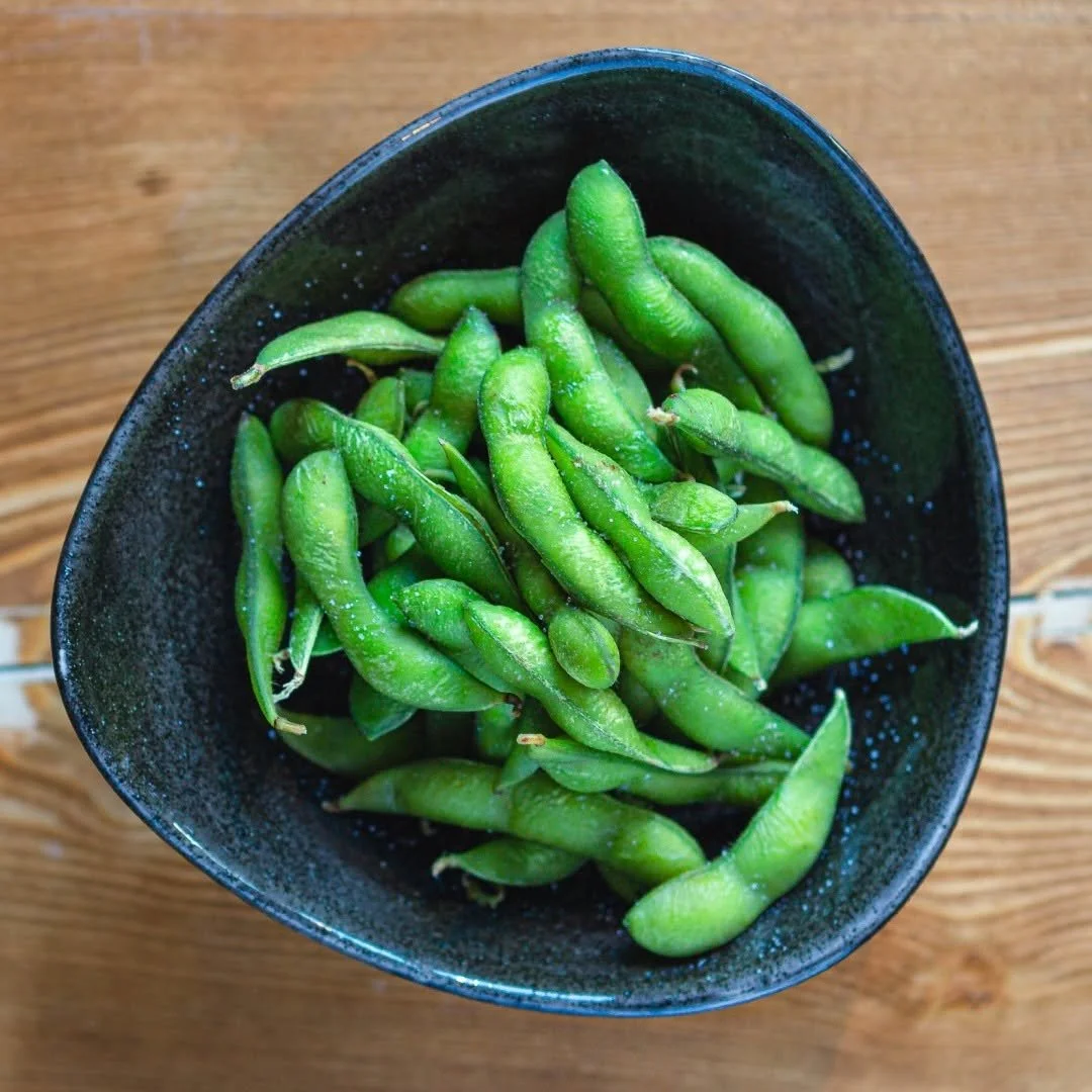 Grüne Edamame in einer schwarzen Schüssel auf einem Holztisch