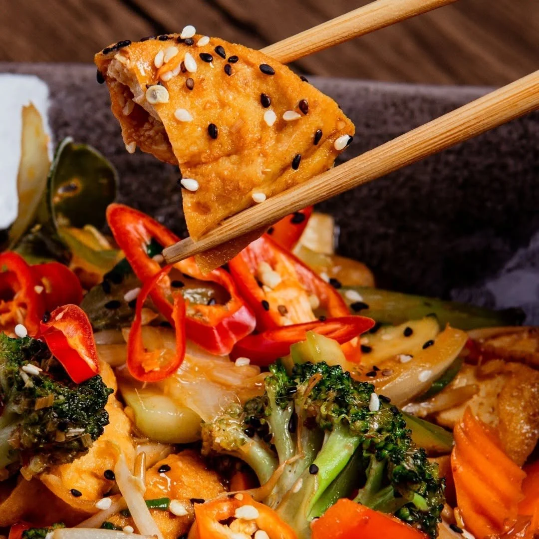 Close-up eines Essens mit paniertem Tofu mit Sesamsamen, Gemüse wie Brokkoli, Paprika, Gurken und Zwiebeln.