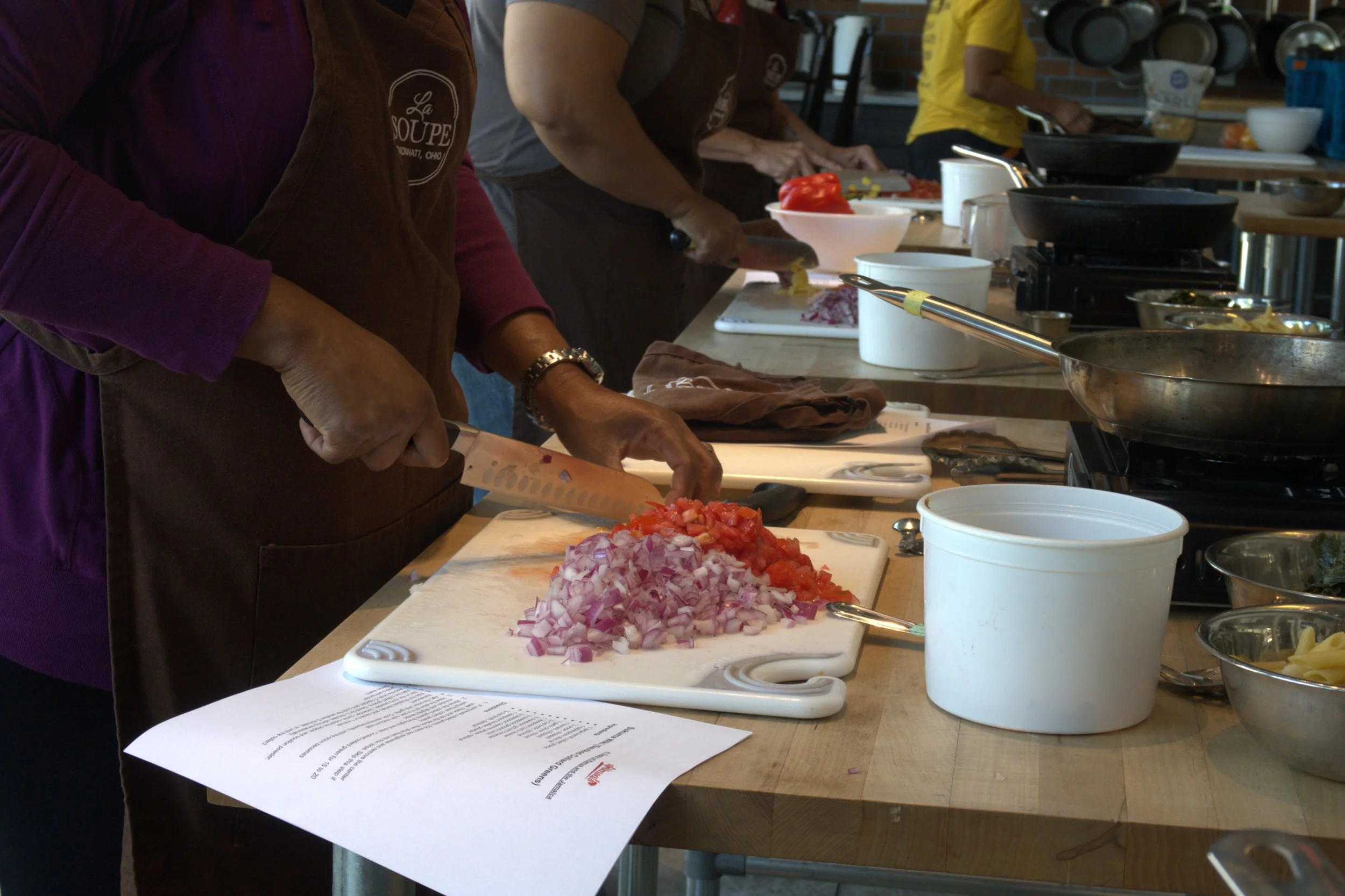 A person chopping tomato and onion on a cutting board.