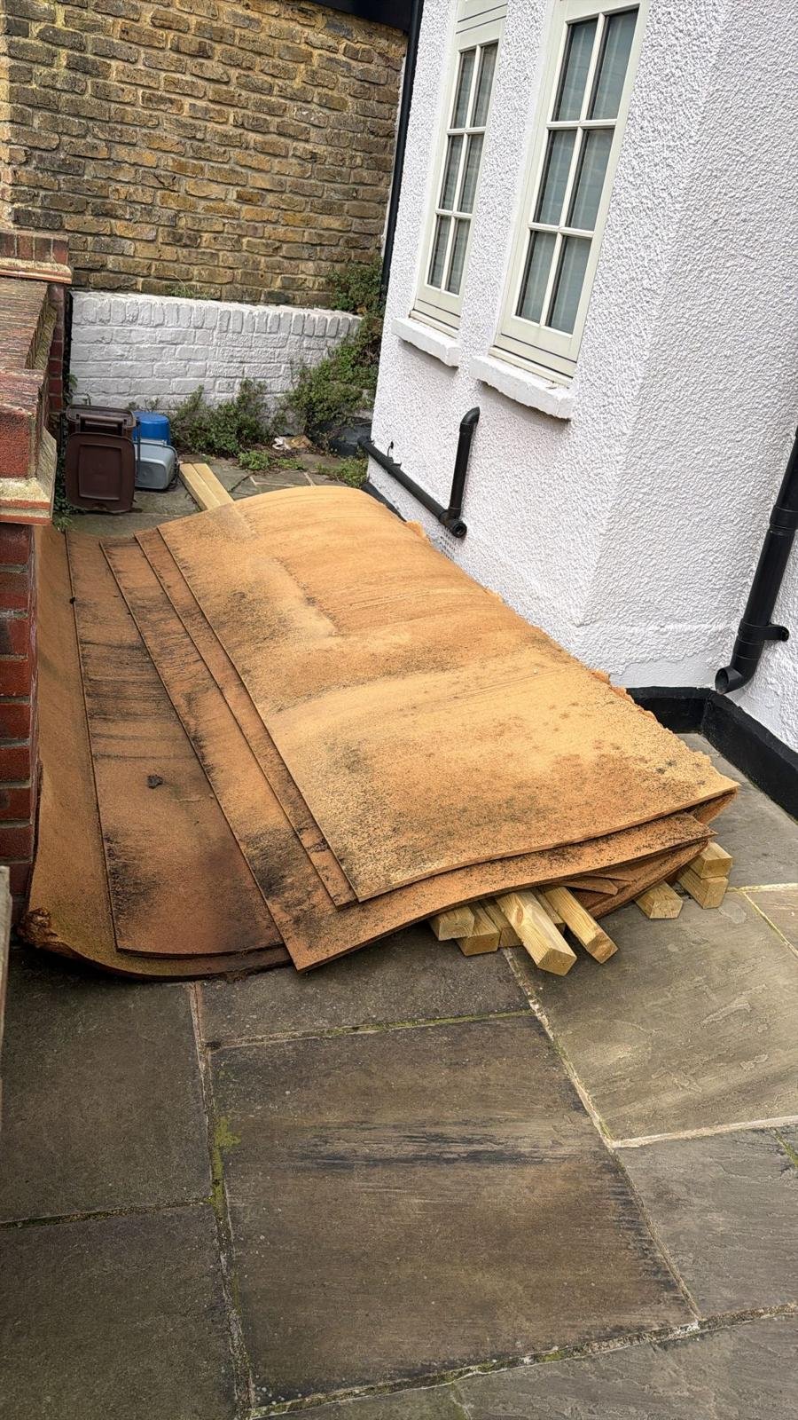 Garden Clearance in Clapham clearing a stack of old wooden roof tiles placed on wooden supports outside next to a white building with two windows.