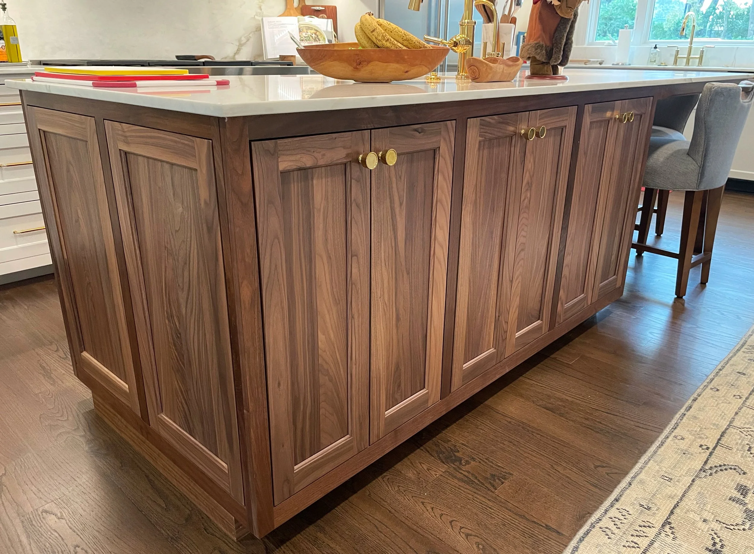 A kitchen island with wooden cabinetry, a white marble countertop, gold hardware, and a bowl of bananas on top.