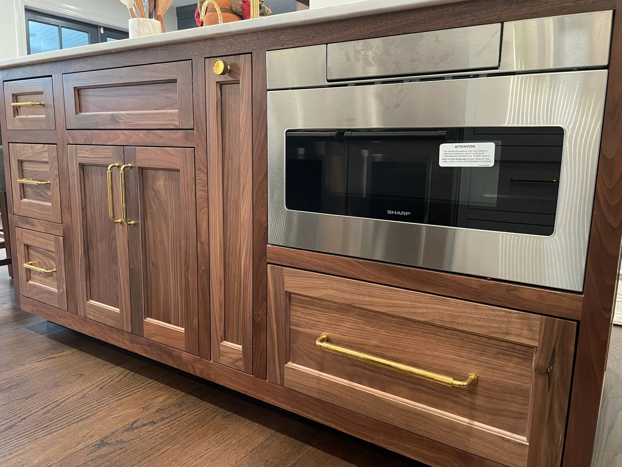 Kitchen cabinet with wooden doors and gold handles, and a built-in stainless steel microwave oven.