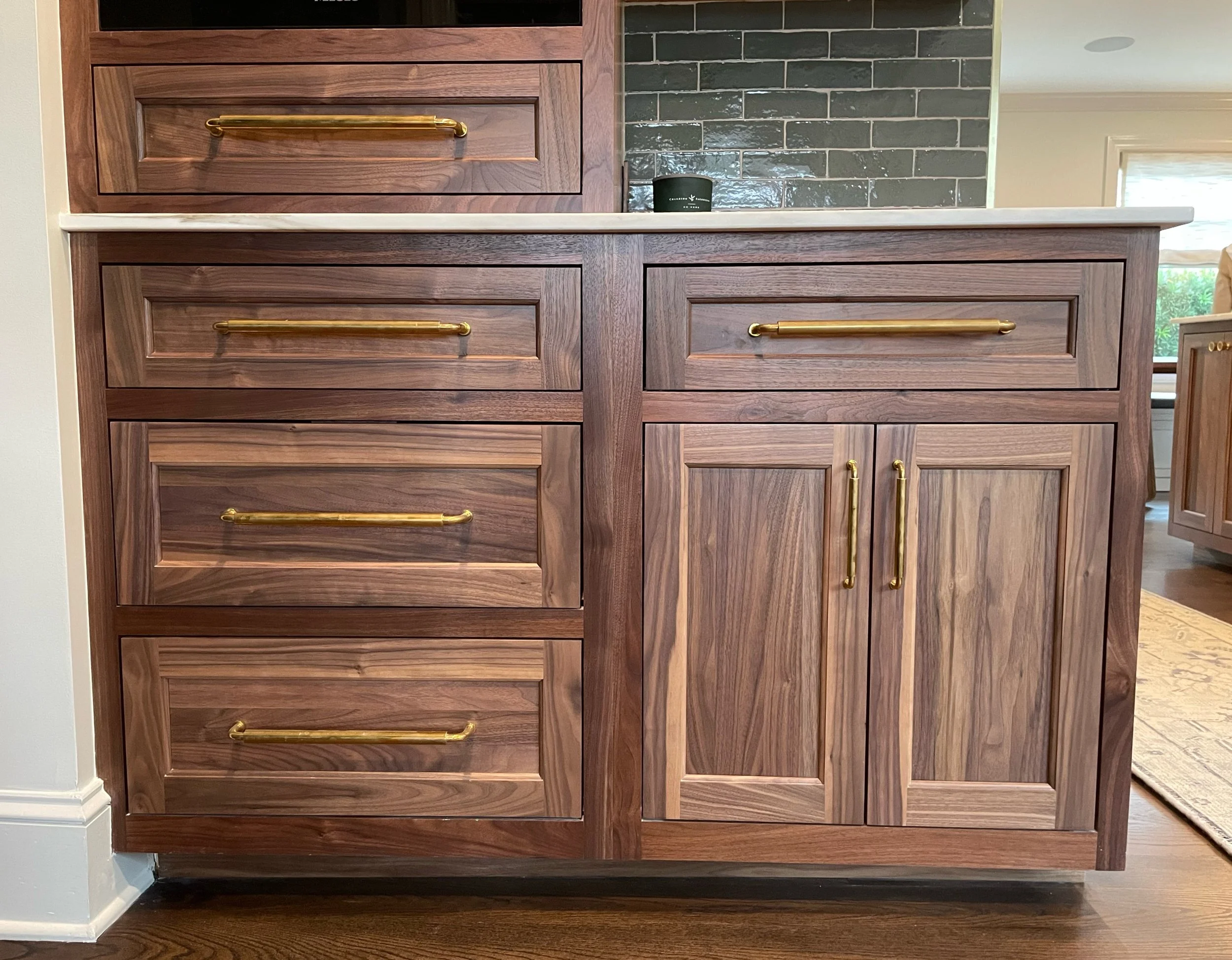 Wooden kitchen cabinet with four drawers and two doors, featuring gold handles, against a brick backsplash and countertop.