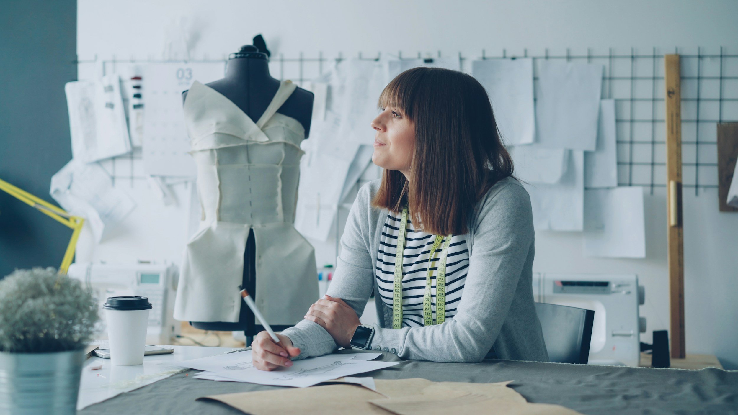 Woman writing a note in a notebook while looking away in deep thought, conveying focus and reflective thinking.