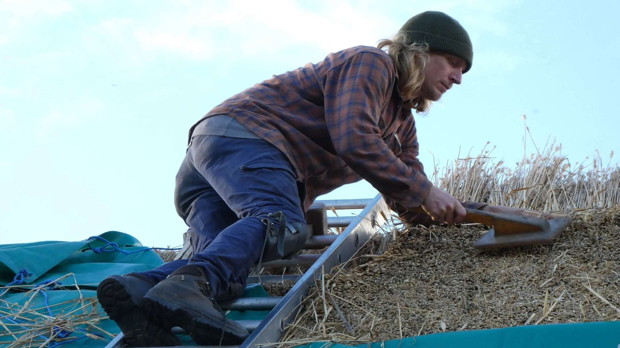 A thatcher using a leggett to dress a thatched roof.