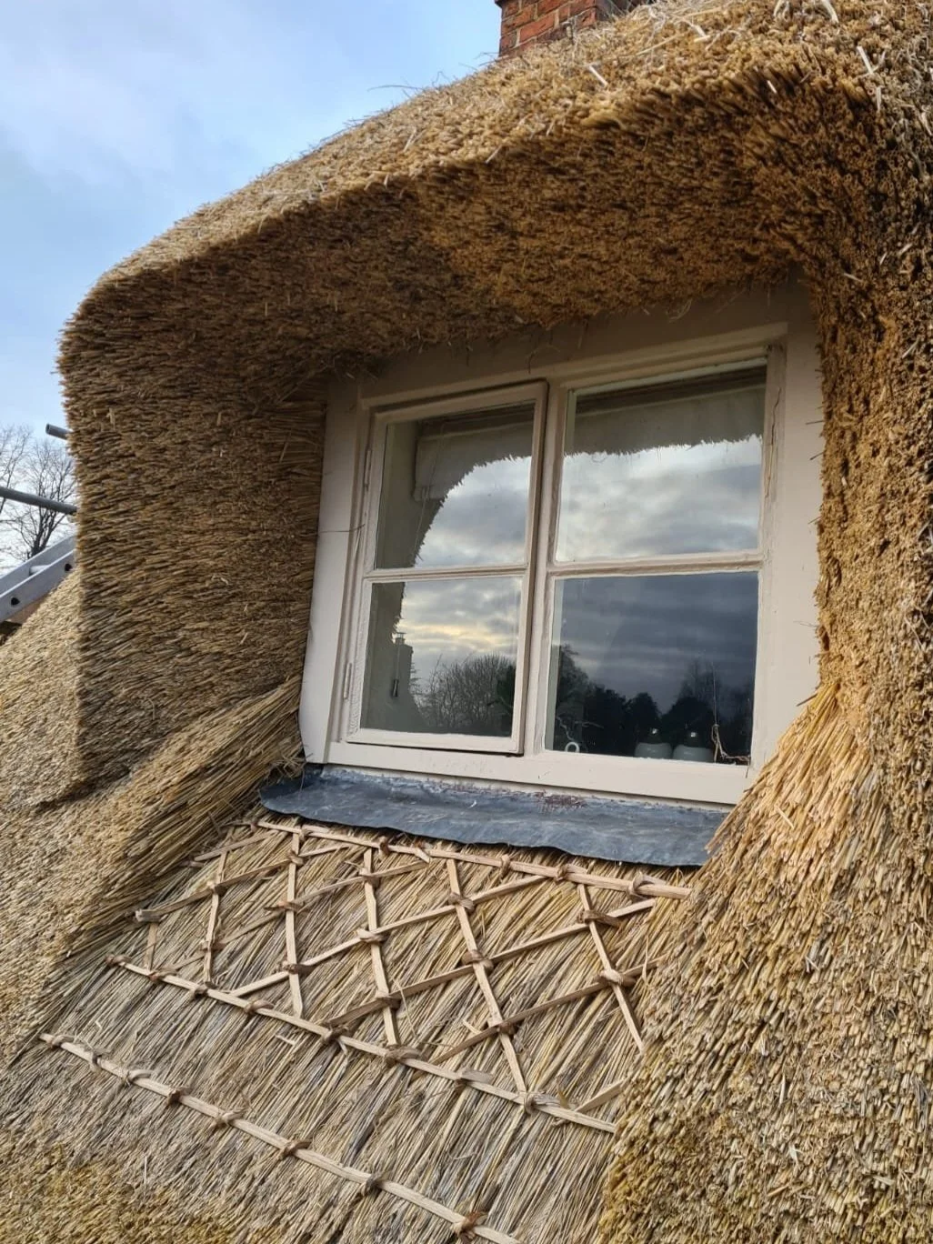 Close-up of an exterior house window with thatched eaves and hazel detailing