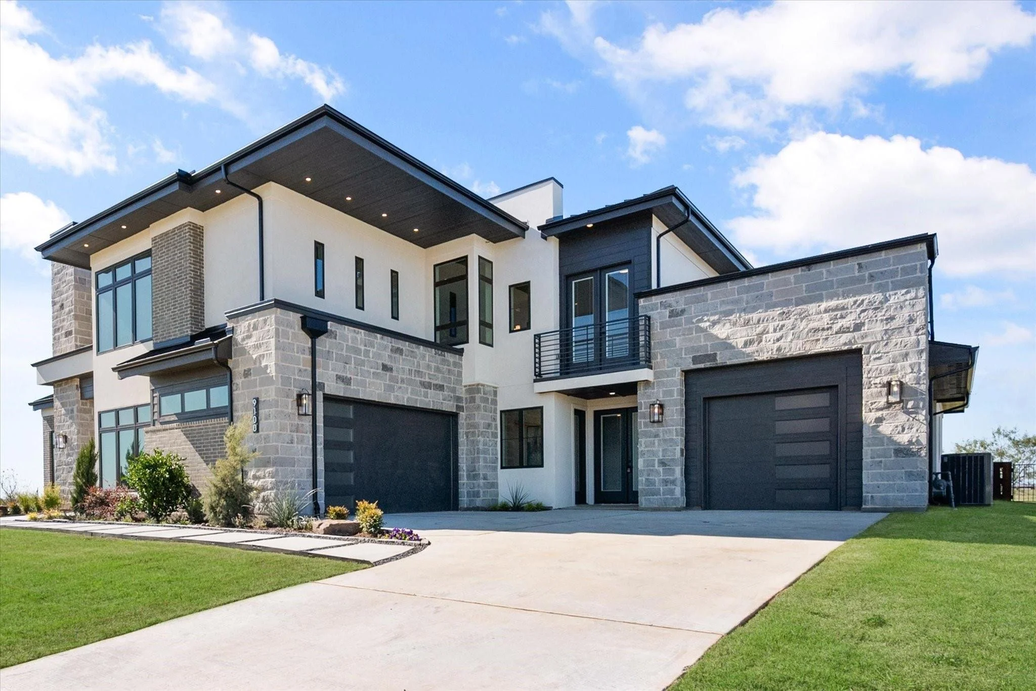 Modern two-story house with a combination of dark gray and white exterior, large windows, and a two-car garage. The home features a landscaped front yard.
