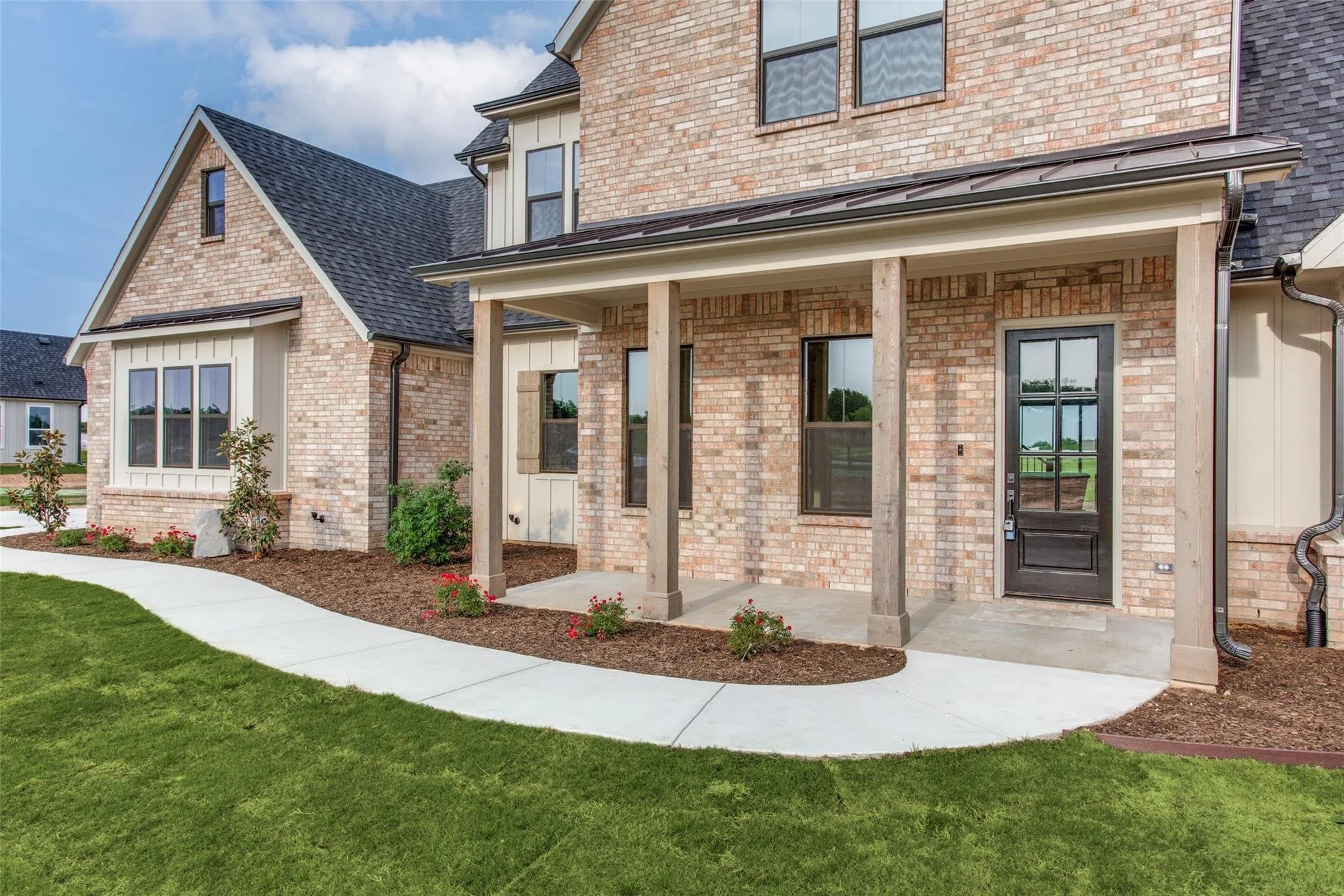 Brick house exterior with covered porch, black windows and door, landscaped yard, and curved concrete walkway.
