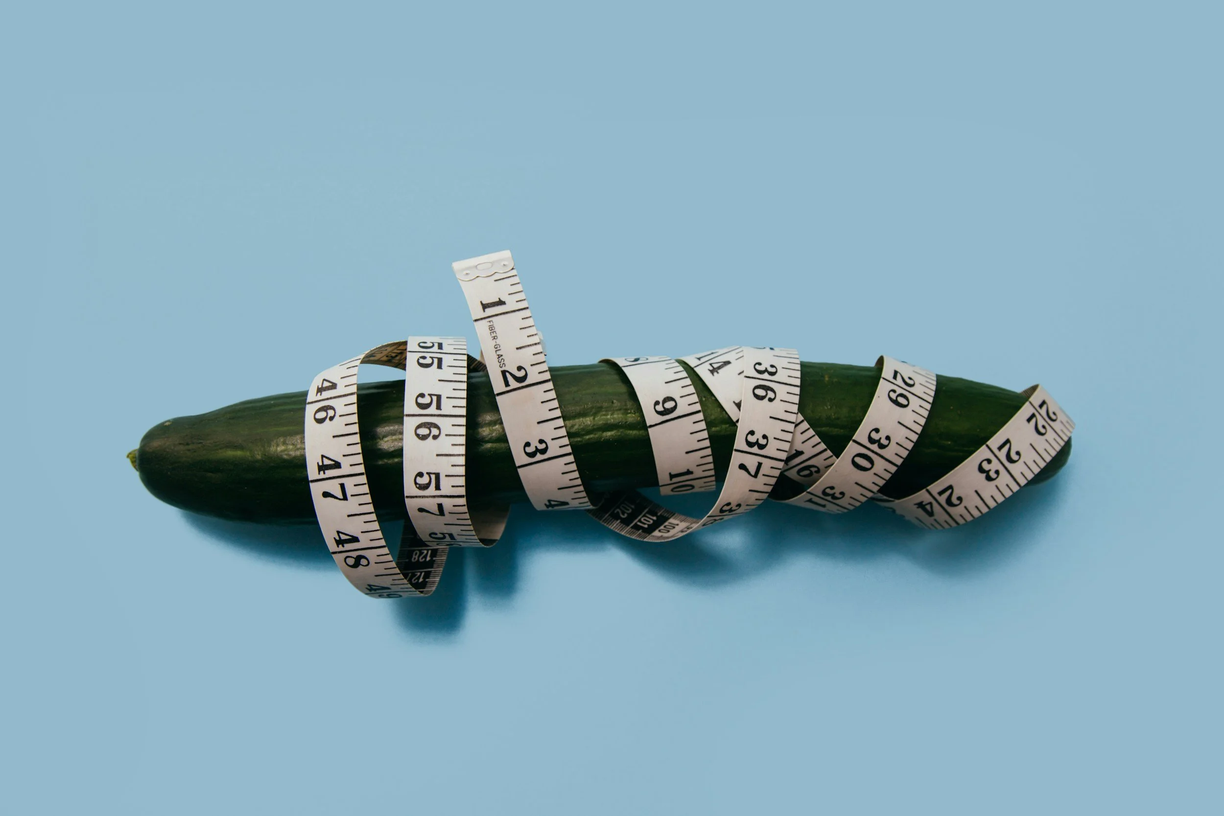 A cucumber wrapped with a white measuring tape, placed on a light blue background.