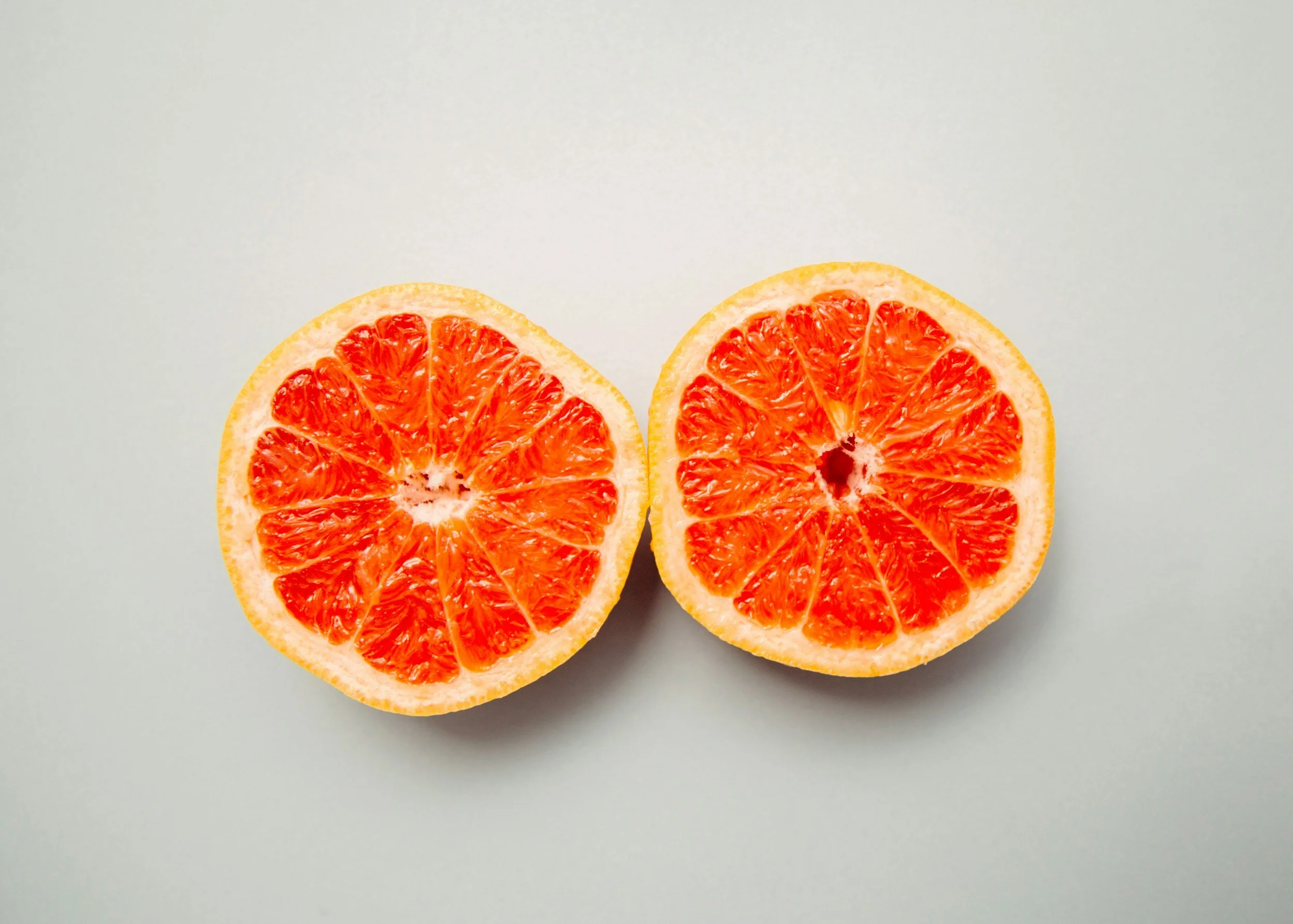 Half of a grapefruit with bright orange flesh, placed on a light-colored background.