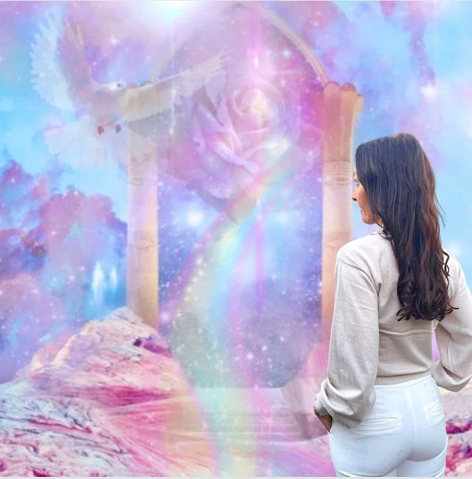 A woman with long dark hair wearing a light-colored sweater and white pants looking at a dreamy, colorful mural with a rainbow, clouds, and celestial elements.
