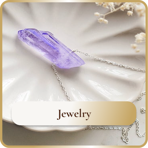 A necklace with a purple crystal pendant on a white ceramic dish, with small white flowers in the background.