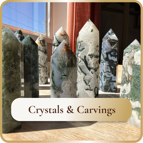Several large decorative crystals or carvings with intricate patterns, displayed on a table near a window, with a sign reading "Crystals & Carvings" in front.
