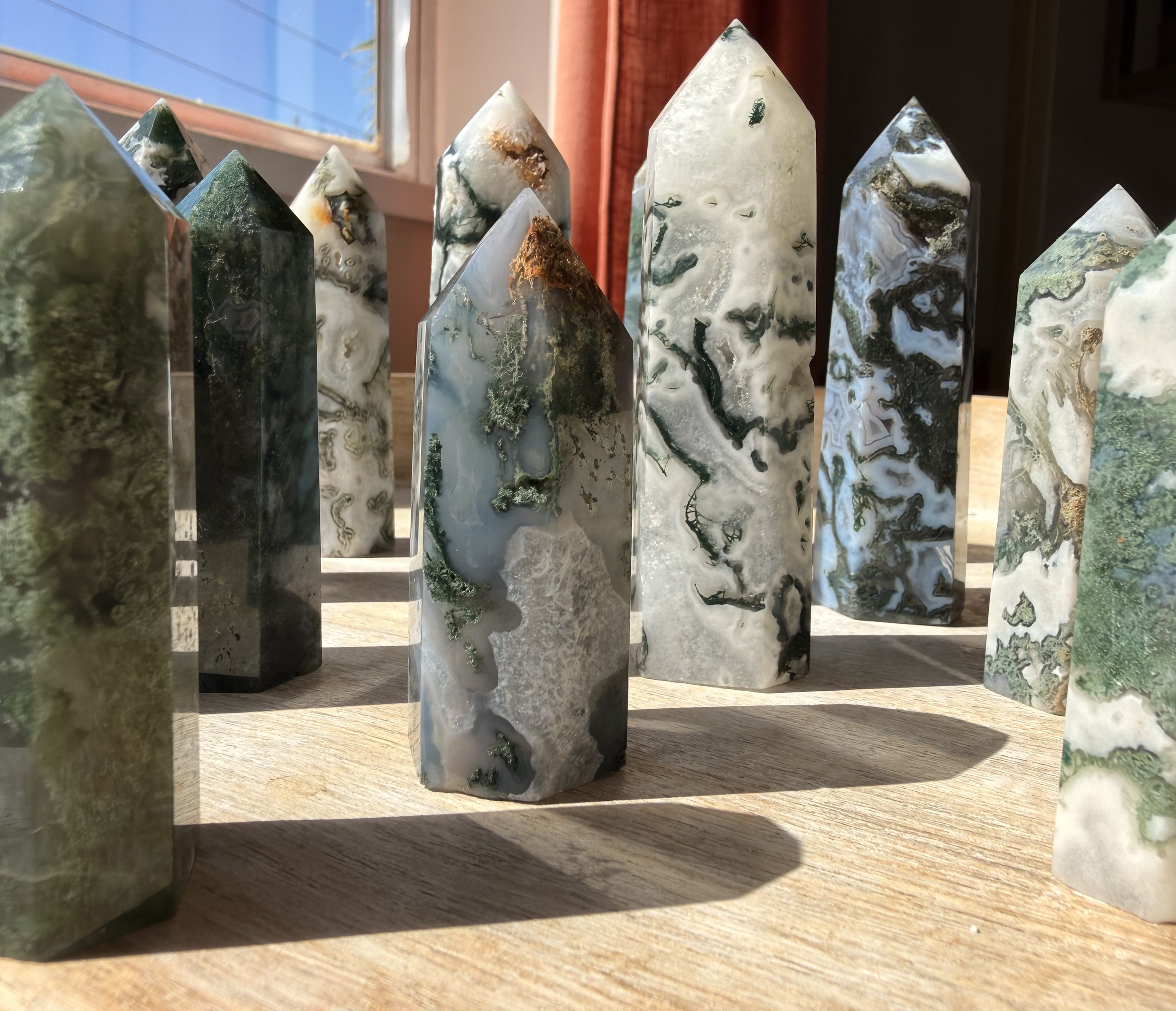 Several polished stone obelisks with green, black, and white marbled patterns arranged on a wooden surface near a window.