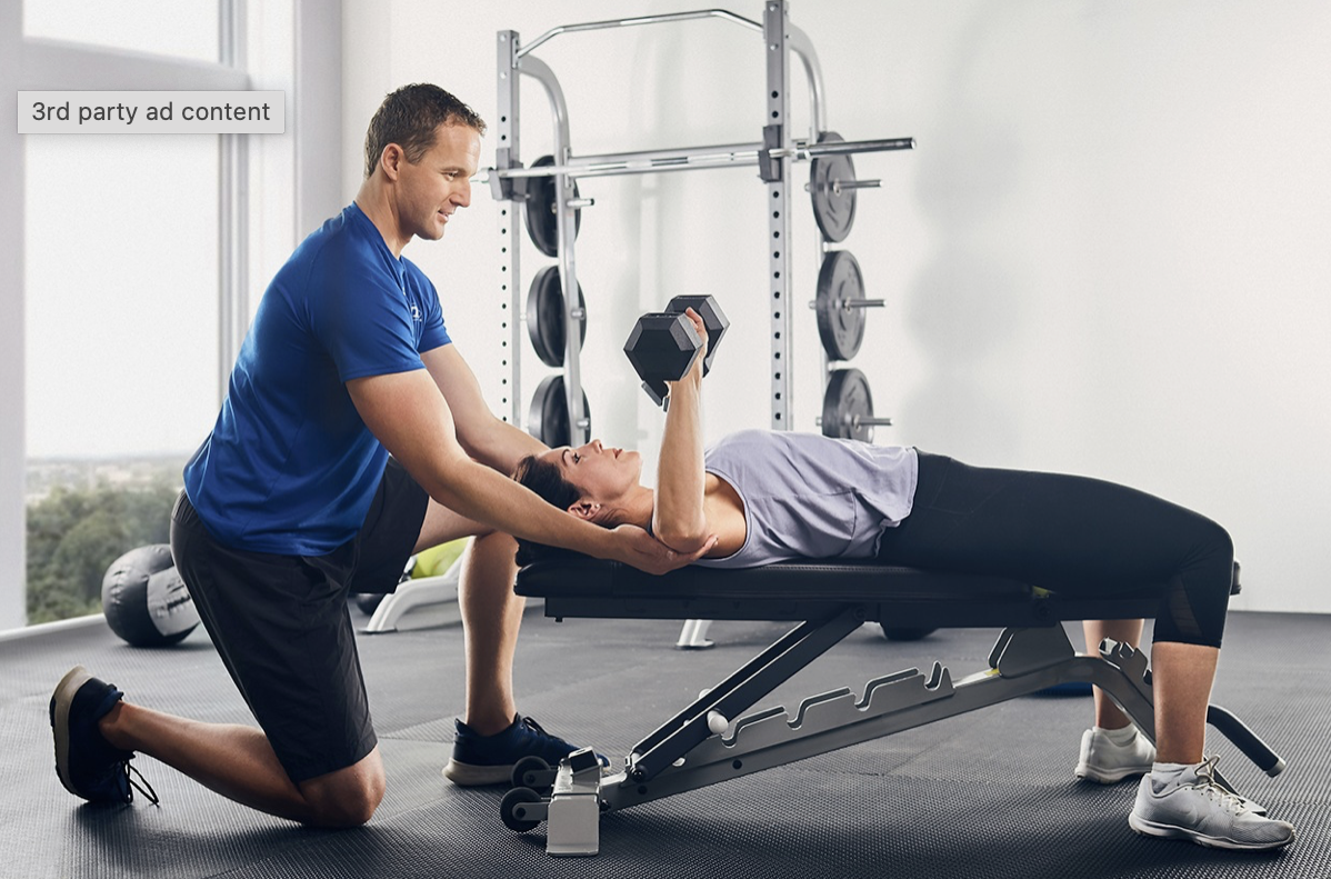 Personal trainer assisting woman lifting a dumbbell during a workout at the gym.