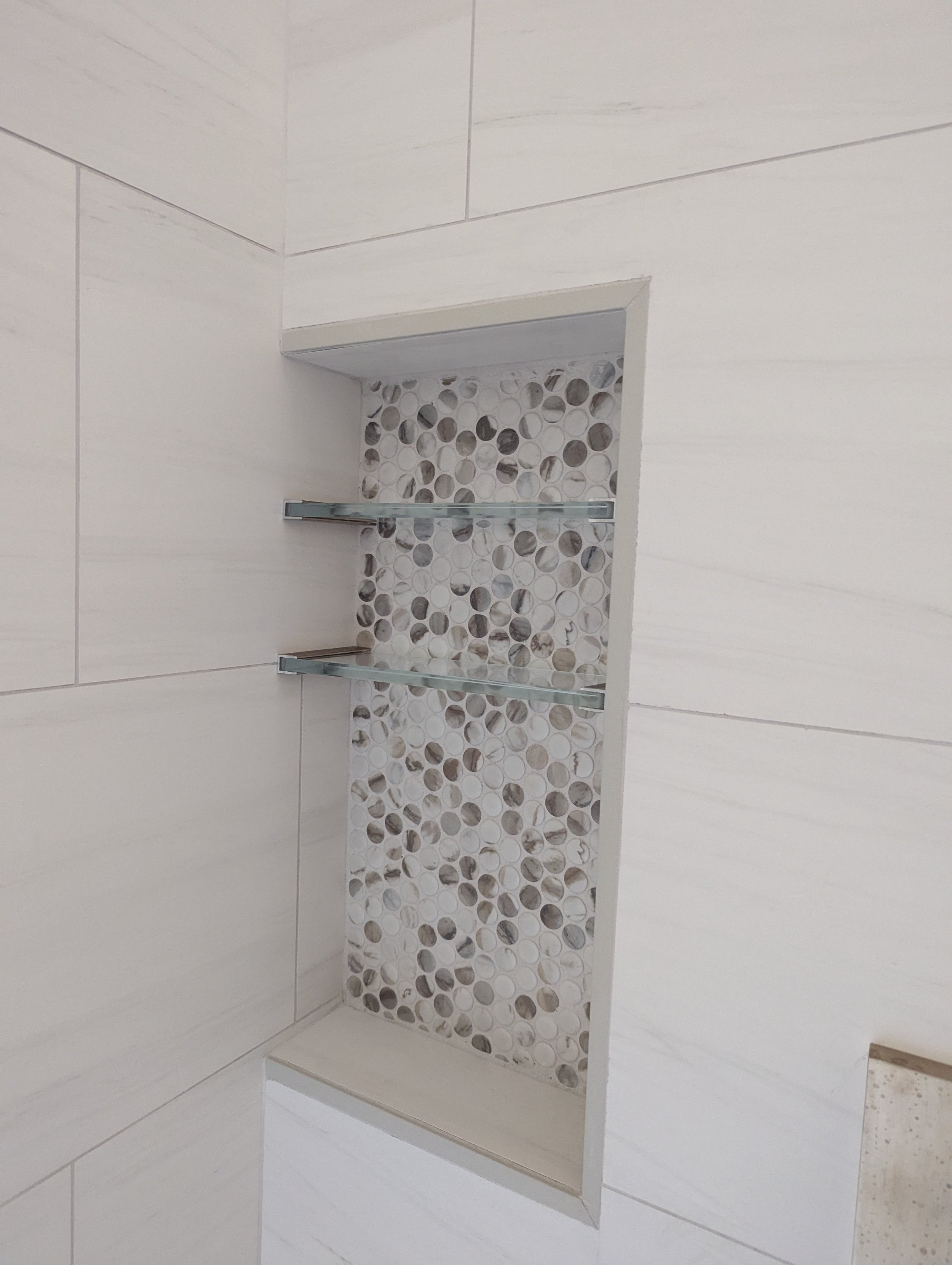 Built-in shower niche with pebble tile background and two glass shelves.