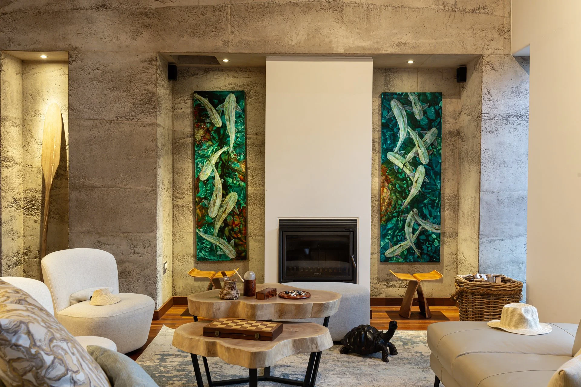 Living room with stone wall, two abstract green and blue art pieces, fireplace, beige furniture, coffee table, woven basket, stuffed turtle, and white hat.