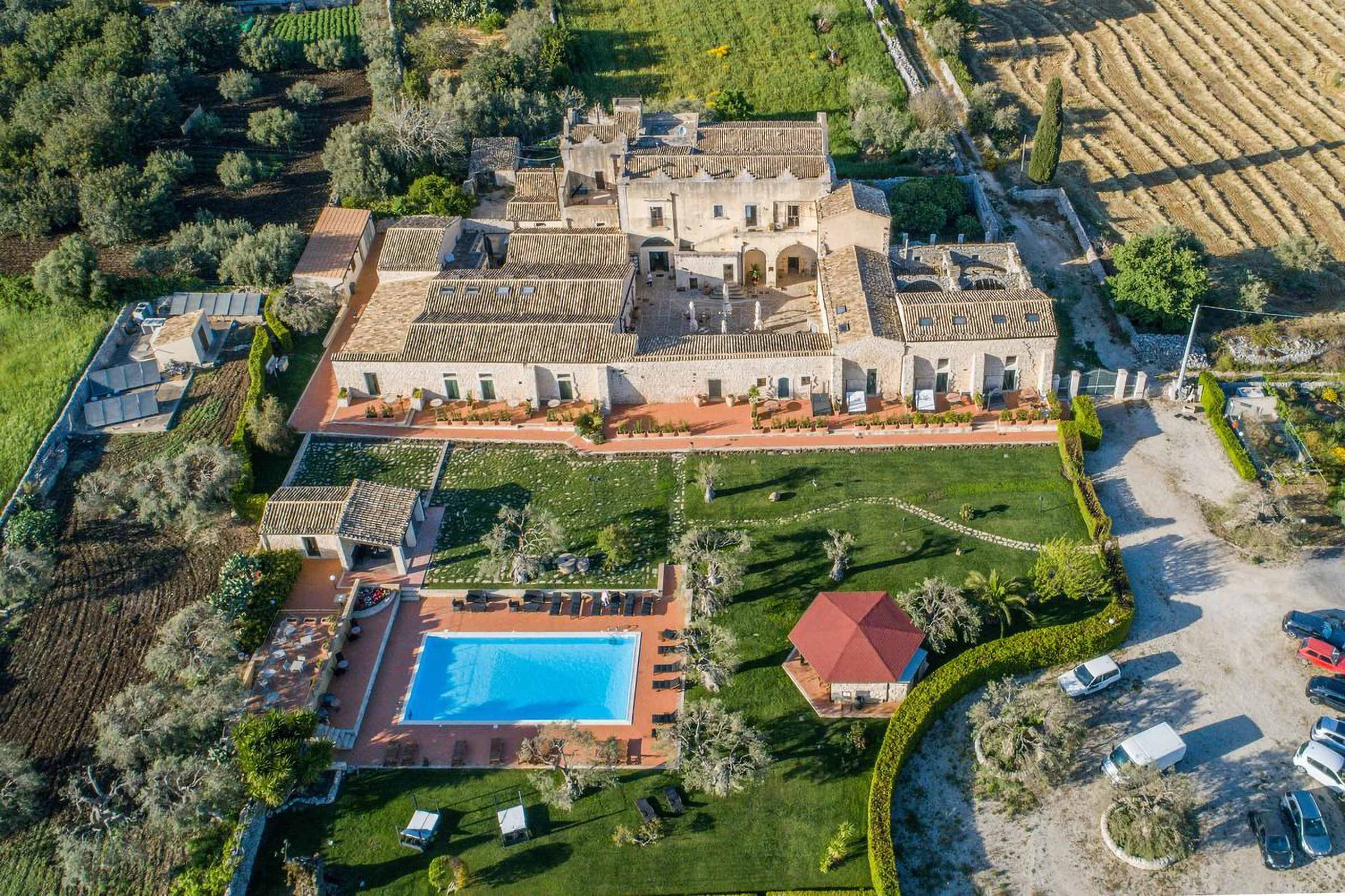 Aerial view of a large Mediterranean-style estate with a main building, swimming pool, garden, parking area, and surrounding farmland and vineyards.