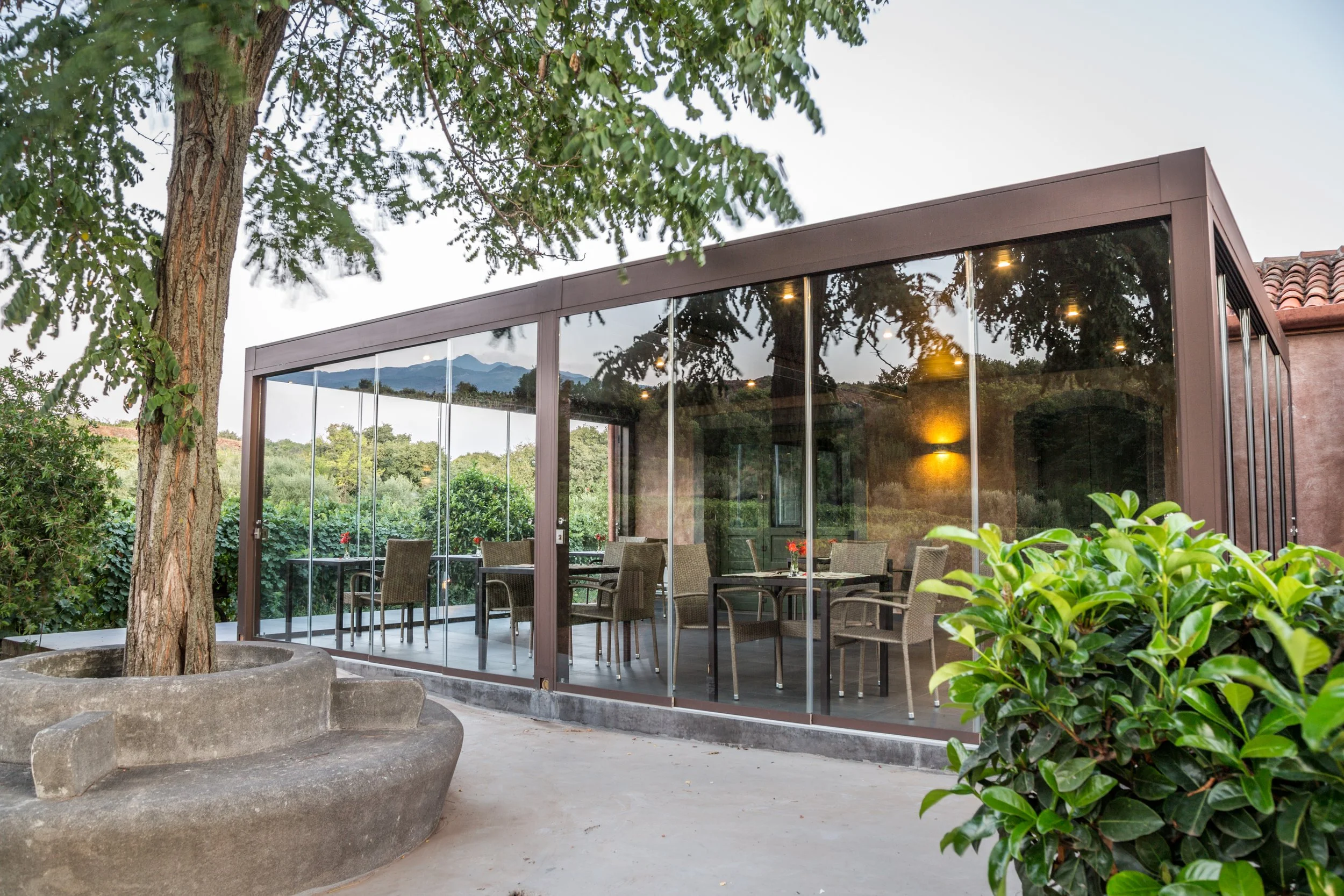 A glass-enclosed patio with outdoor furniture and trees in the background.