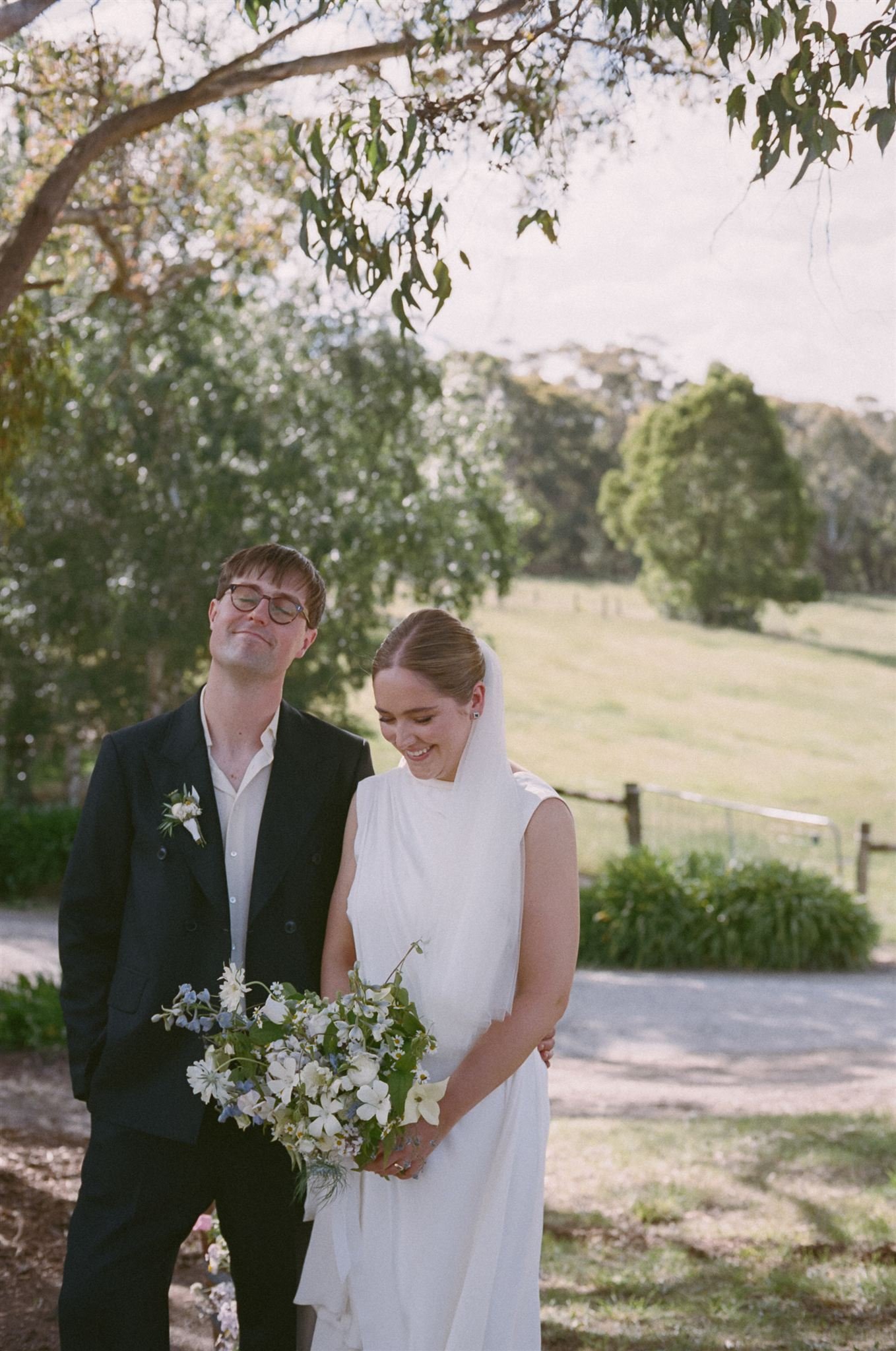 A bride and groom stand together during an outside ceremony, they are smiling and are in a country side setting. 