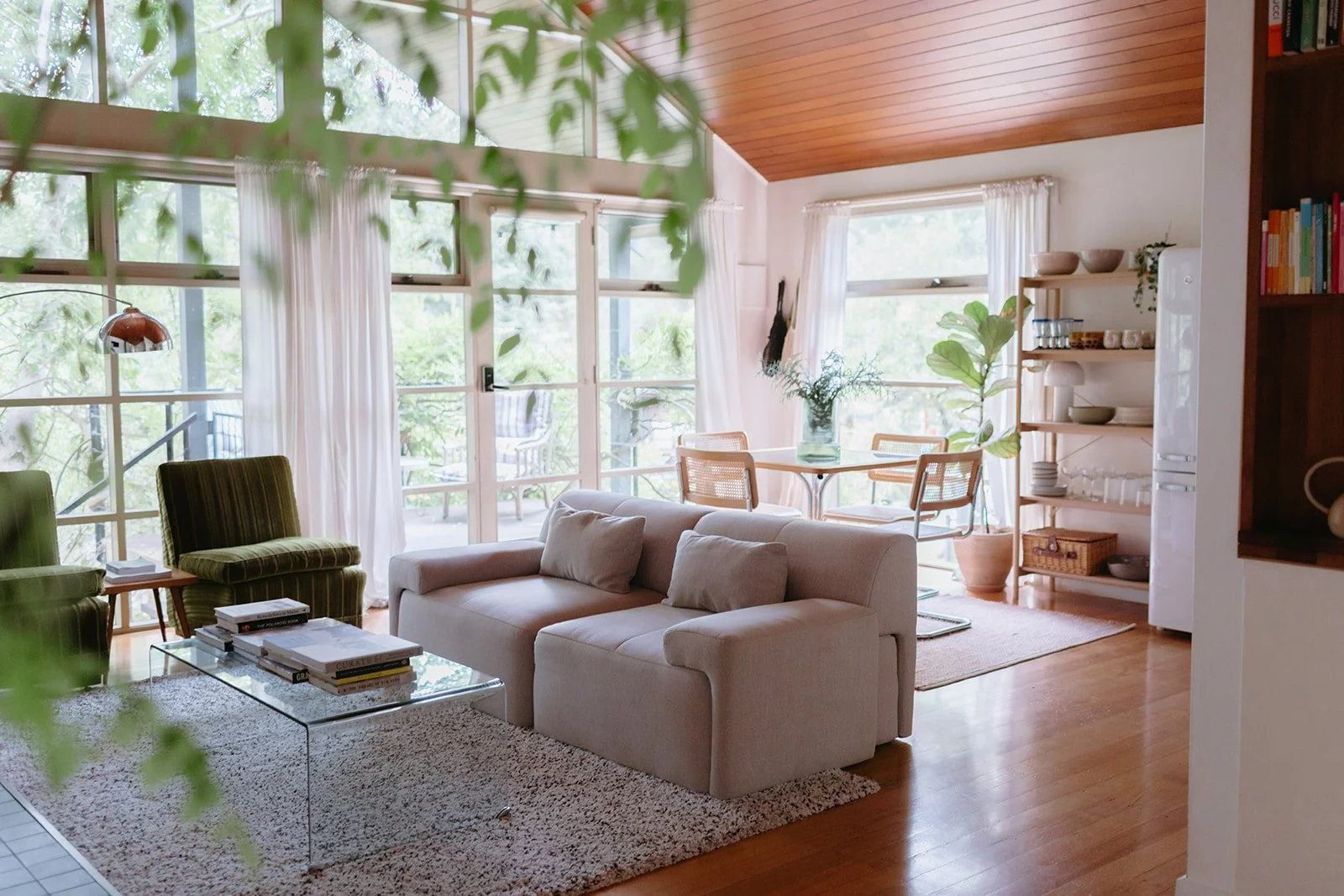 a lounge room with sun streaming through big windows, a stylish couch and round table sit in the background.