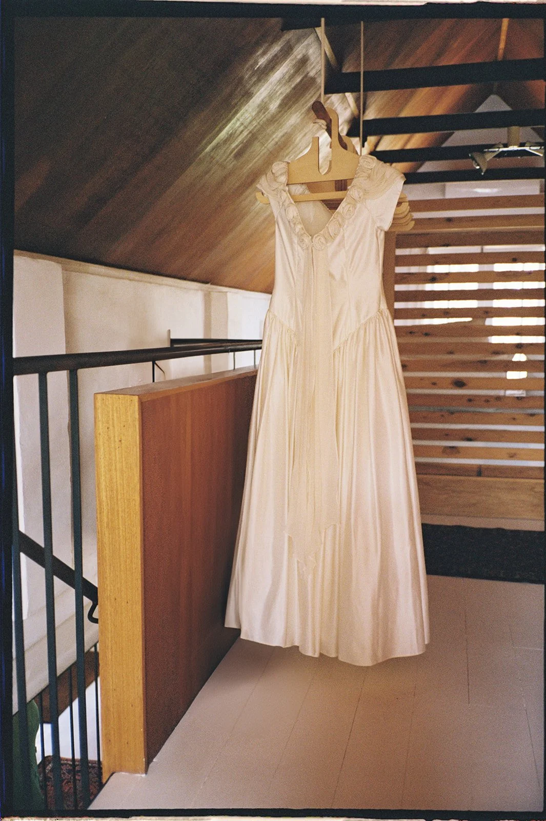 A vintage bridal dress hanging in a bedroom against warm light.
