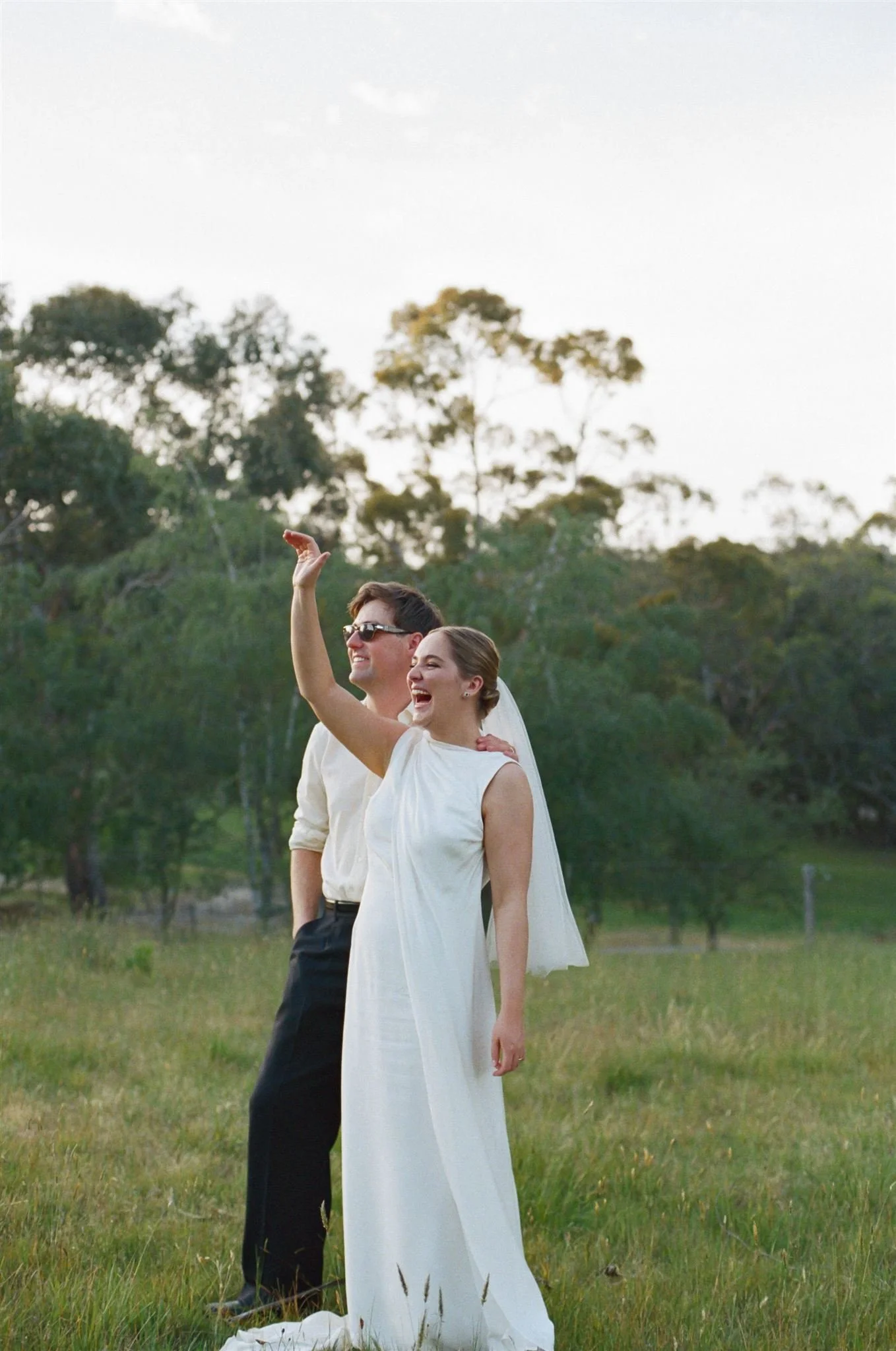 A bride and groom at dusk waving at their guests.