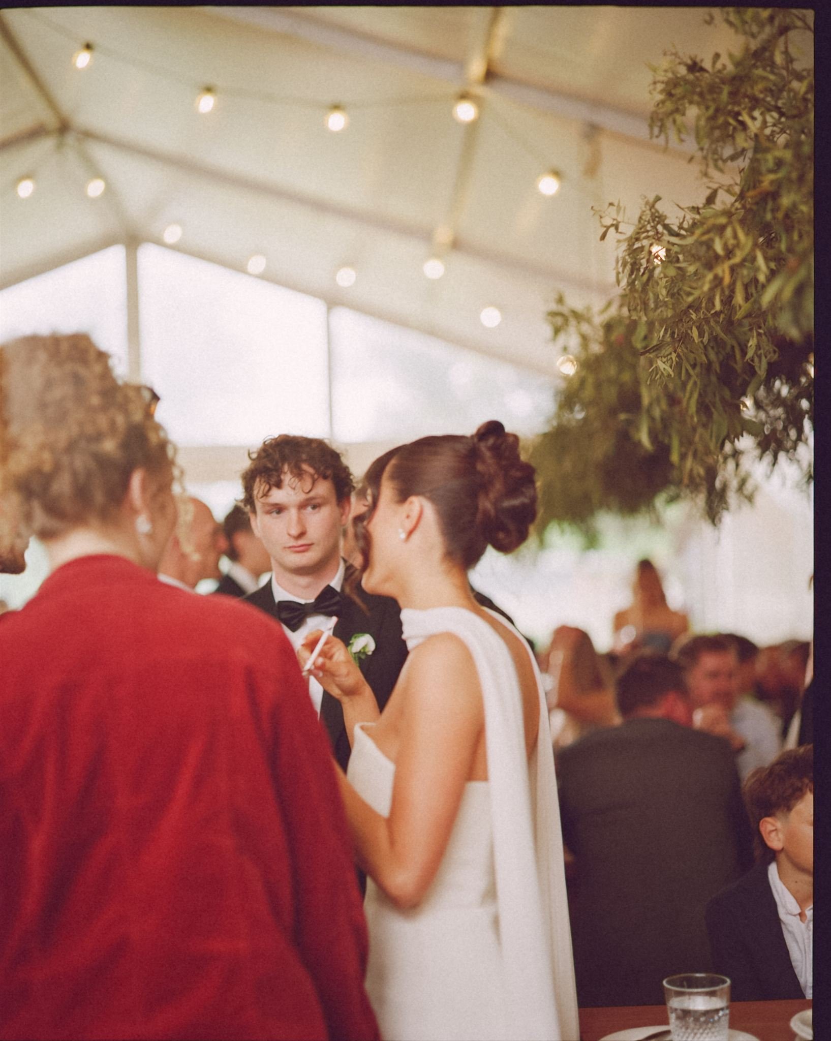 a bride and groom stand at their wedding reception speaking with guests, there are festoon lights in the background.