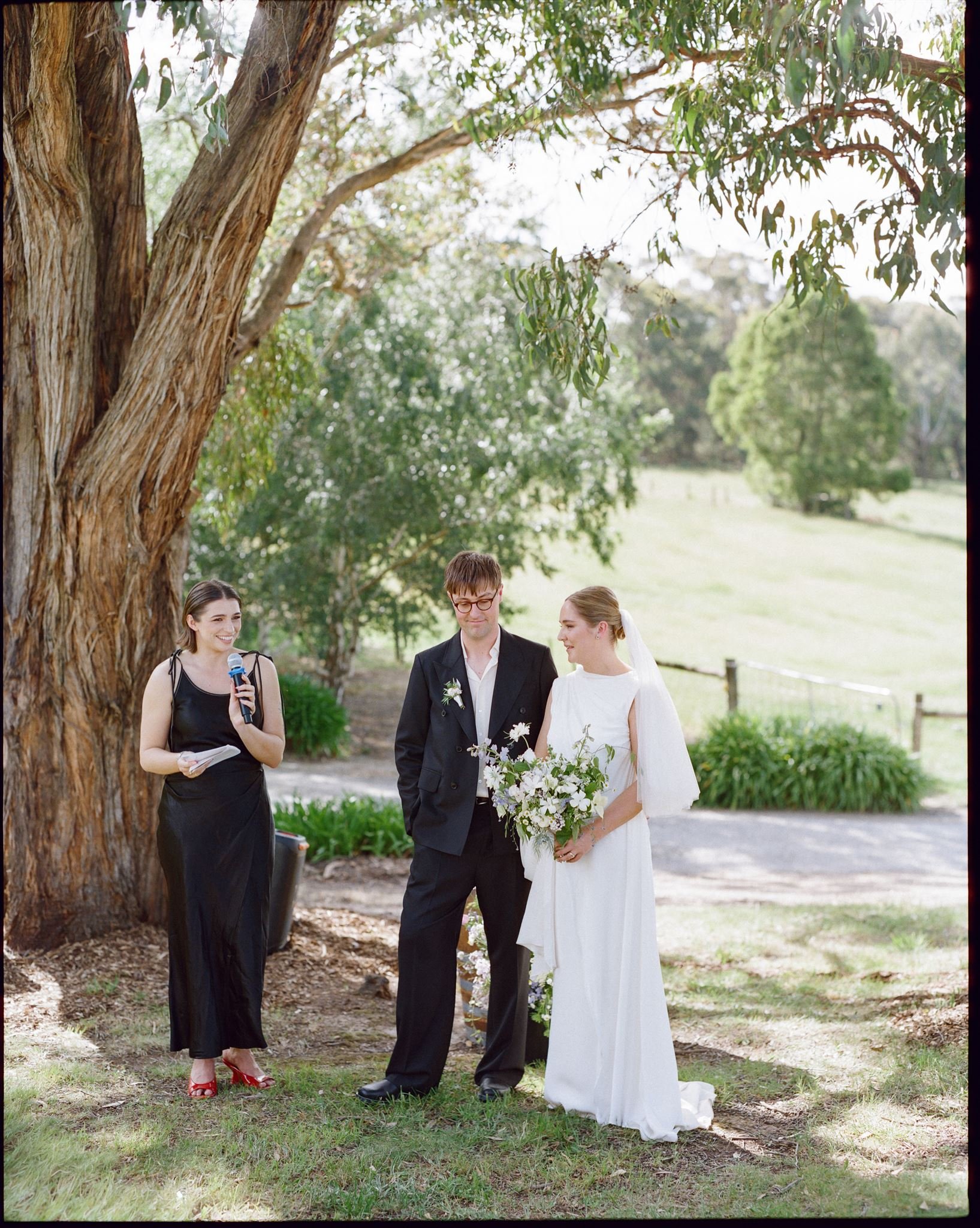 Outdoor micro wedding ceremony in regional Victoria with celebrant, bride and groom beneath a gum tree.