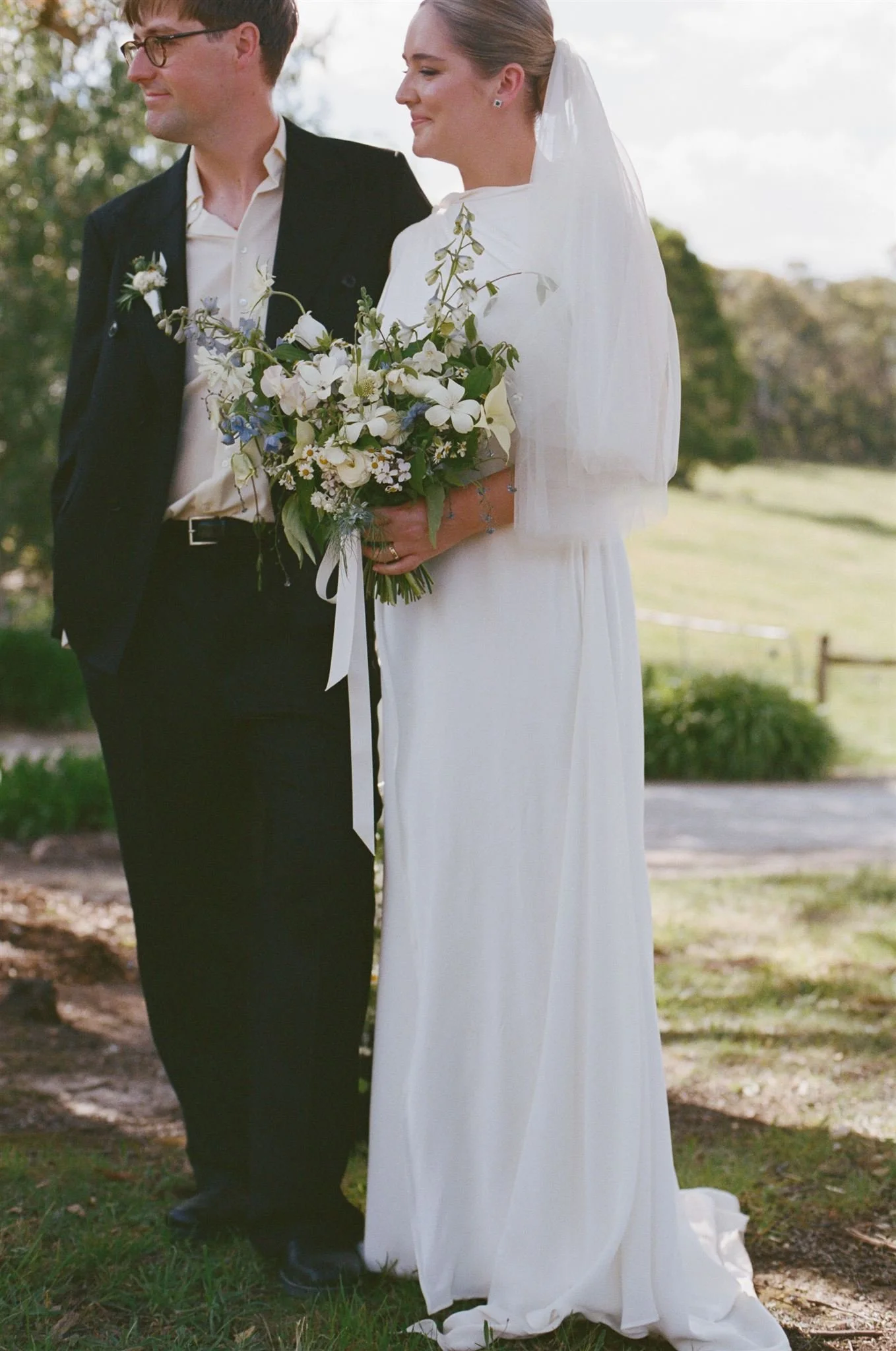 A film photograph of a bride and groom standing in front of a dam during their ceremony.
