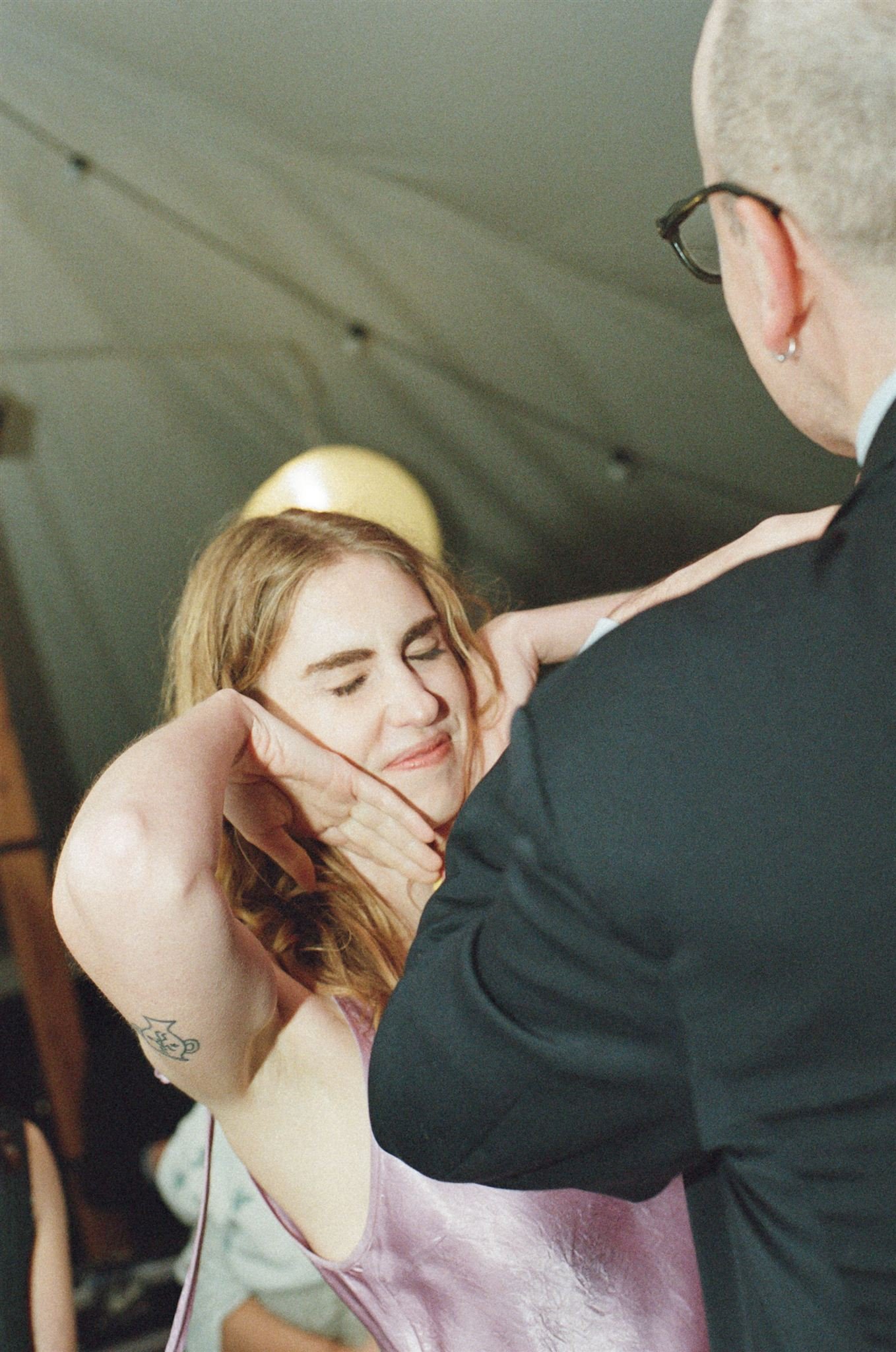 A wedding guest dances inside a reception tent, she is smiling and wearing a lilac silk dress.