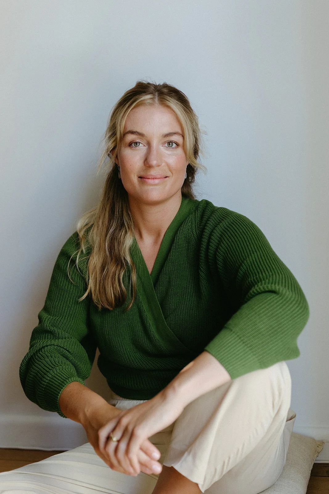 headshot of a blonde women in a green cardigan, looking relaxed in window light.