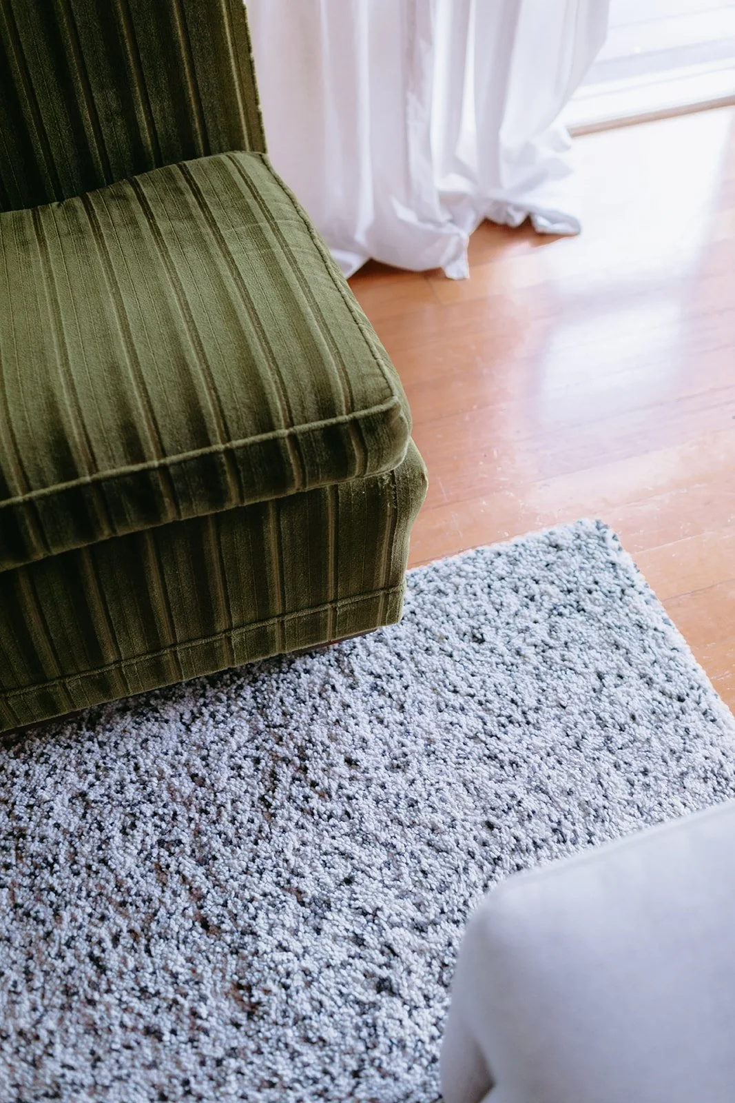 the corner of a green velvet couch and a light grey couch, sitting on a rug.