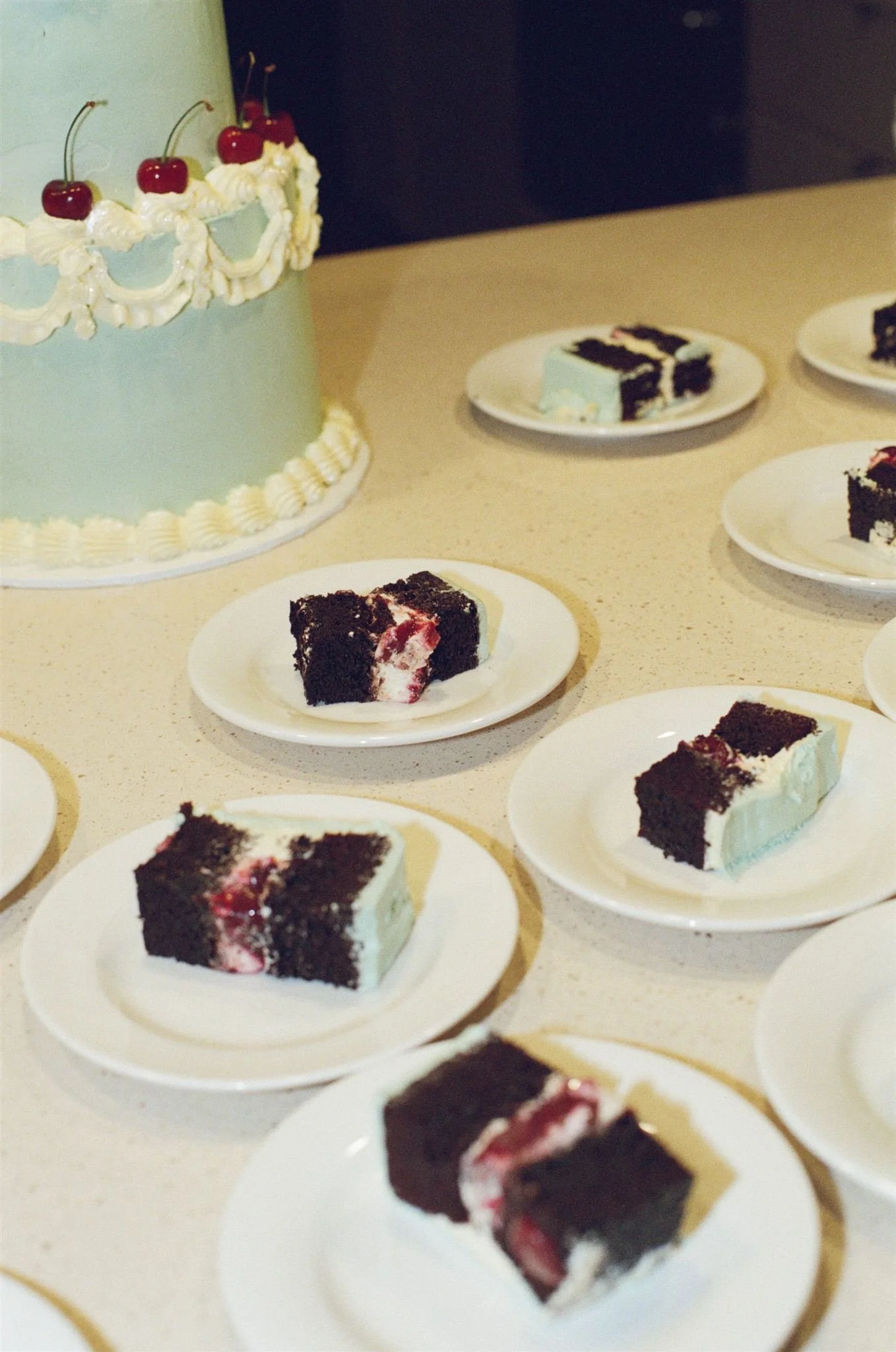 A wedding cake is cut up and plated on a table. The cake looks like chocolate with cherries and buttercream in the middle, with blue icing. 