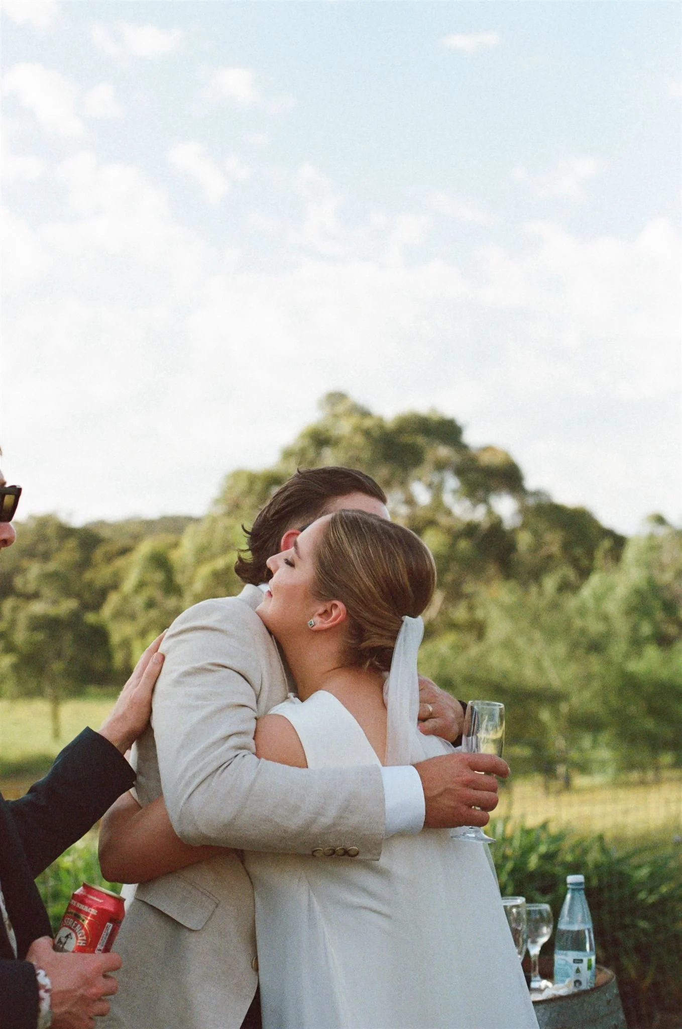 A bride is hugging a wedding guest at an outdoor reception. 