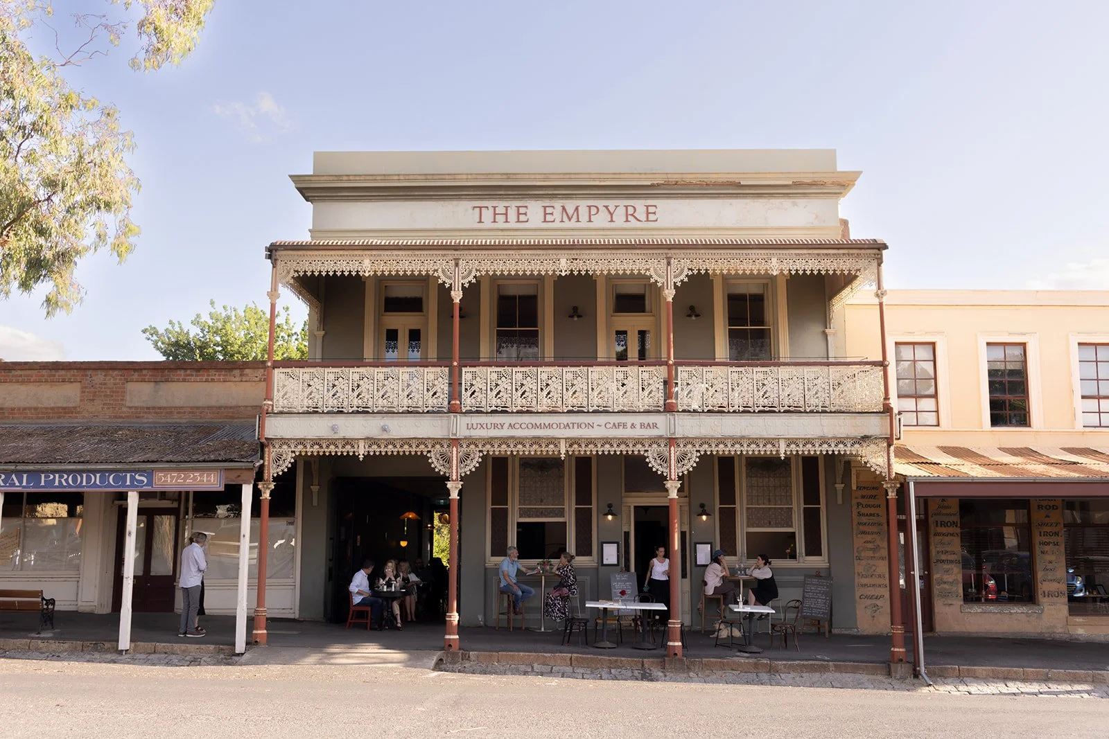 a historic building with terrace balcony, people sits out the front at tables eating food and drinking wine, the sky is blue in the background.