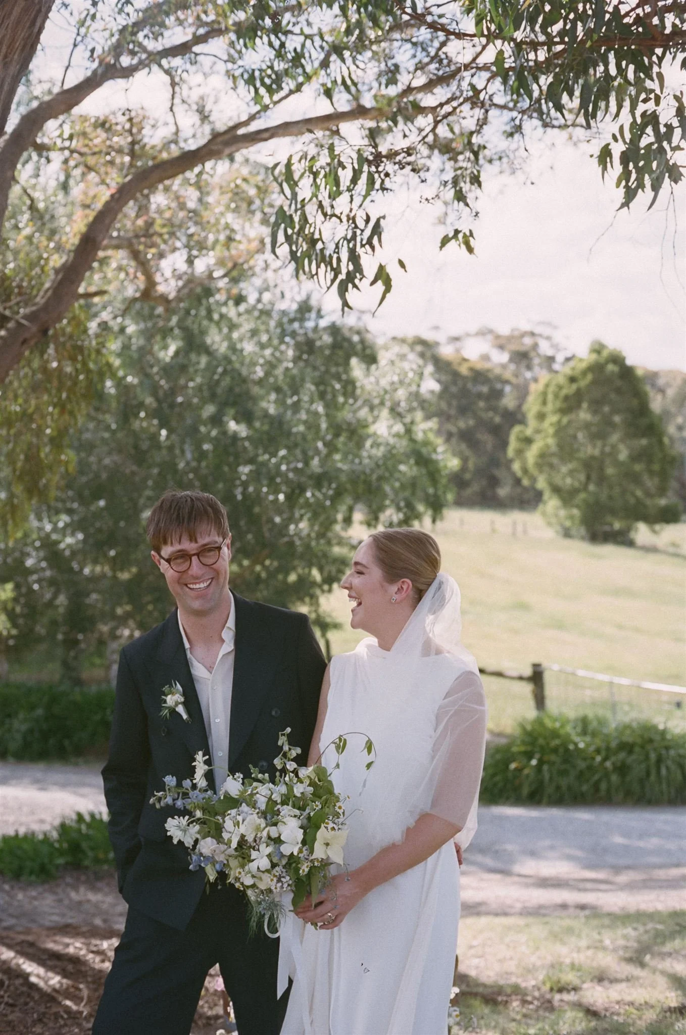 A bride and groom stand together during an outside ceremony, they are laughing and are in a country side setting. 