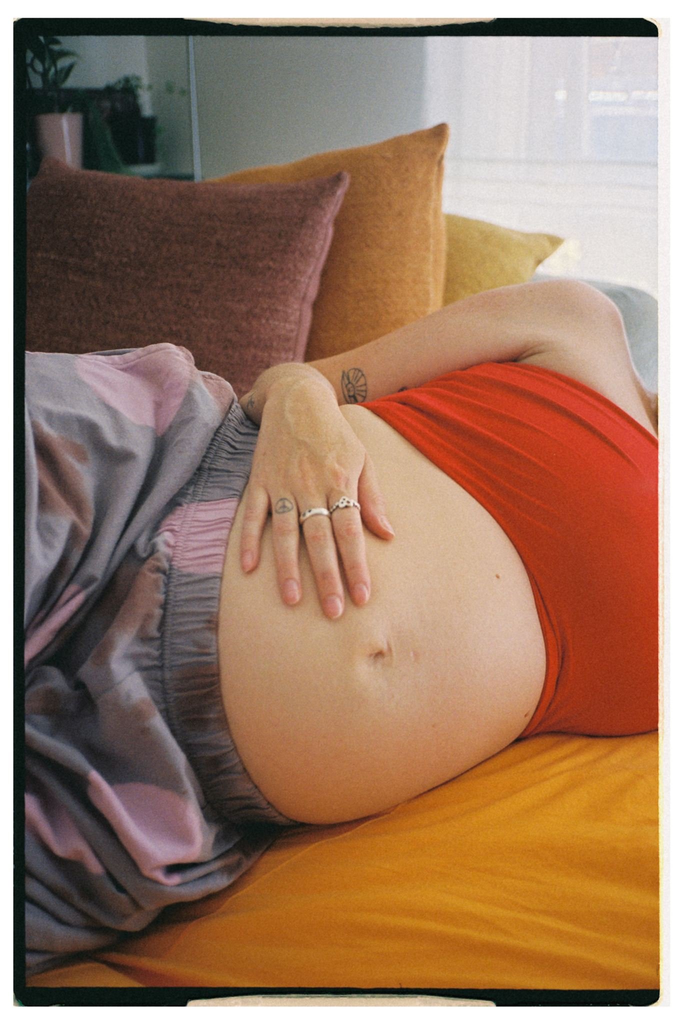 a pregnant women lays on a couch holding her bump, she has silvers rings on and a red top.