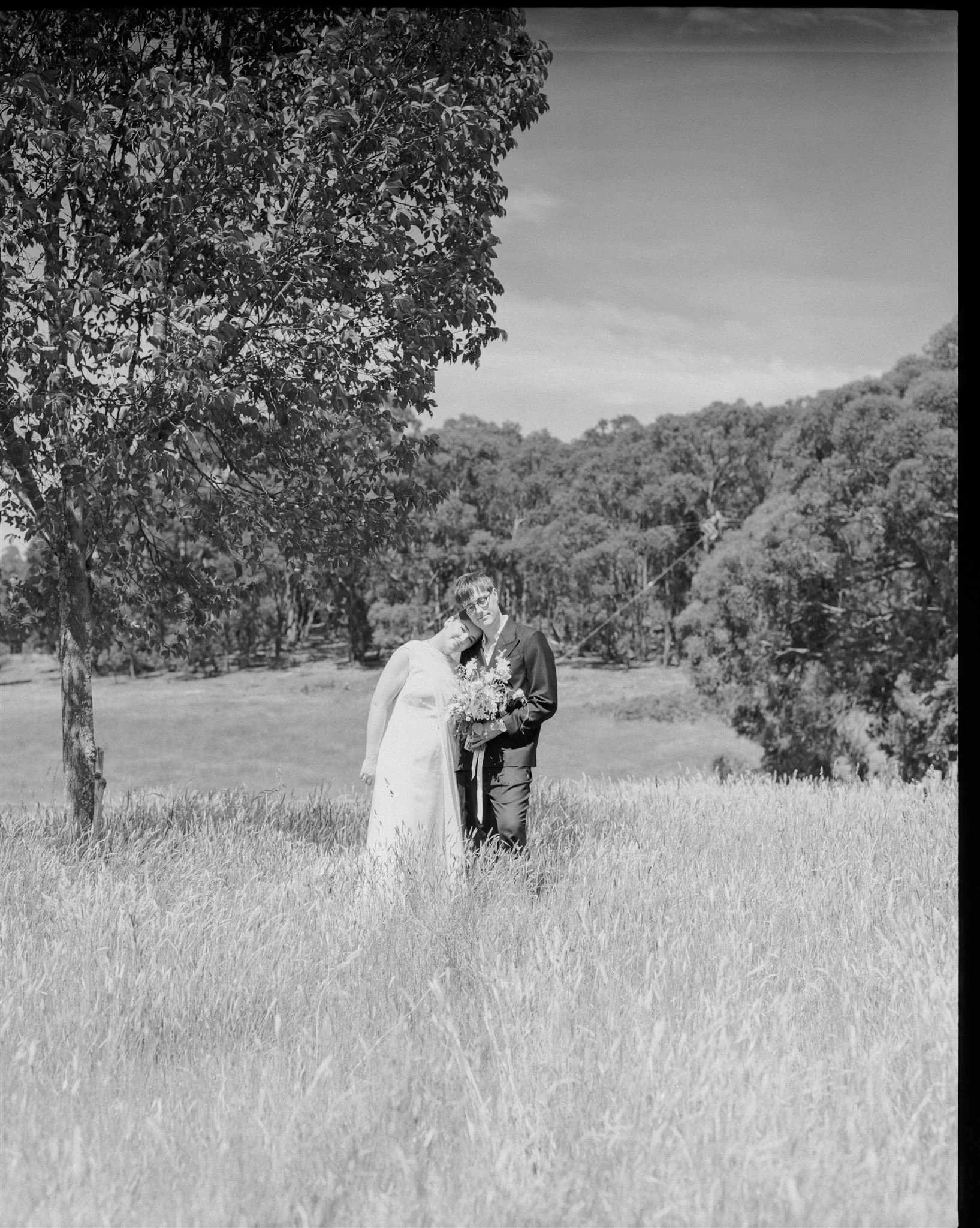 A film photograph of a bride and groom standing in long grass.