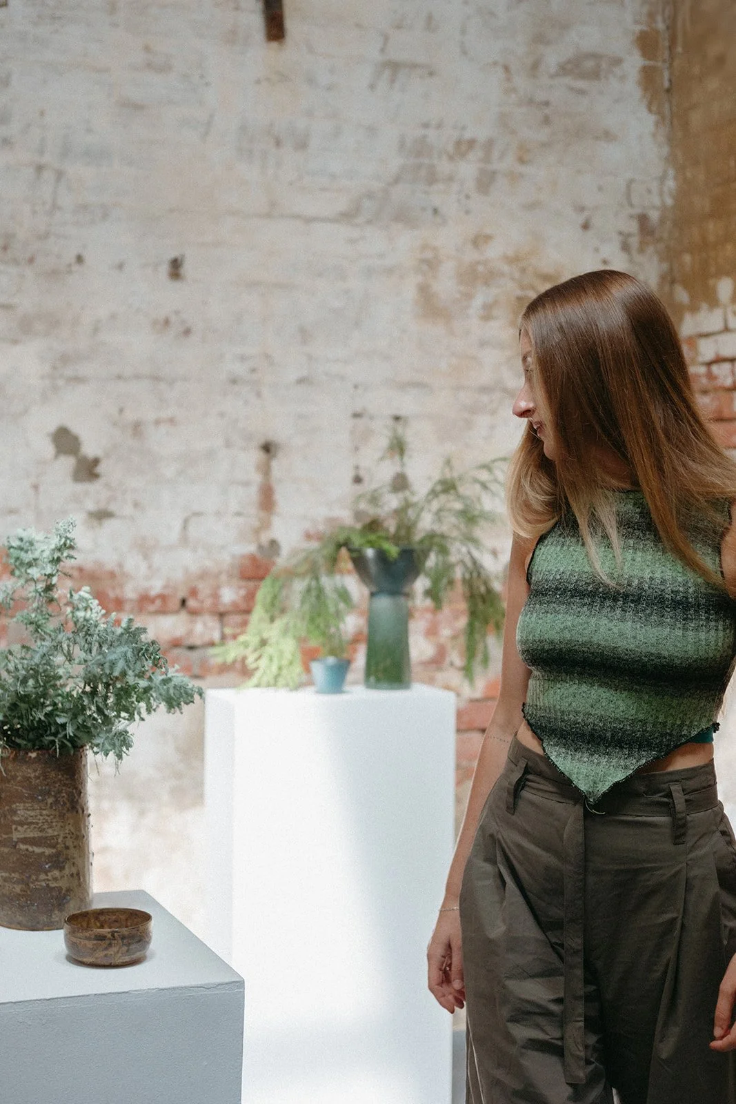 A women stands in an art gallery in Kyneton, she is looking at ceramics while sun streams through a window.