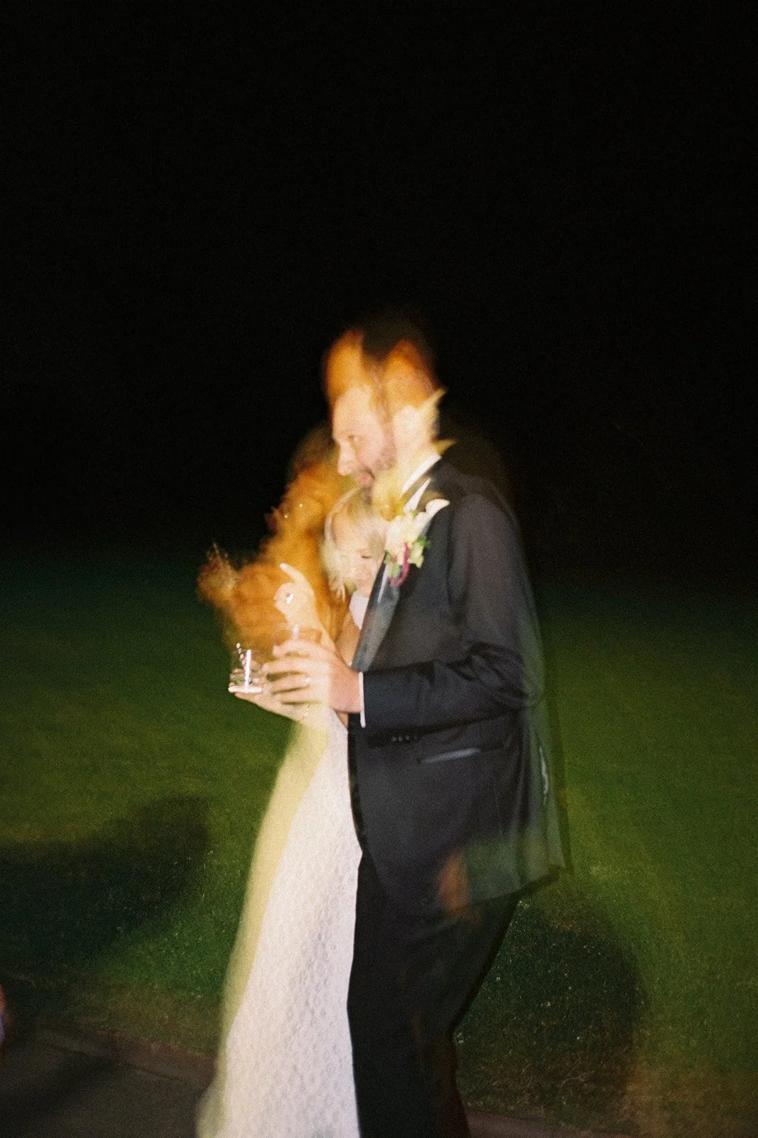 A wedding couple dances outside at night, the photo is taken on 35mm film and there is some motion blur. 