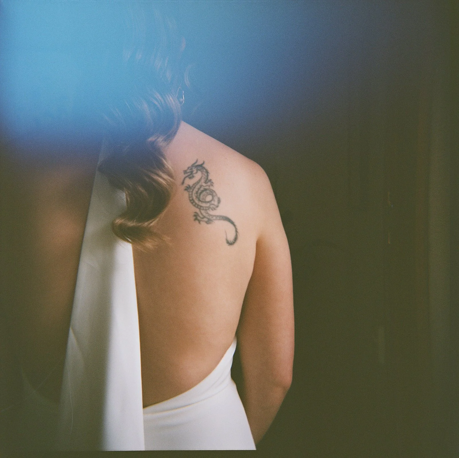 The back of a brides wedding dress, she has a tattoo on her shoulder and a wavy ponytail. 