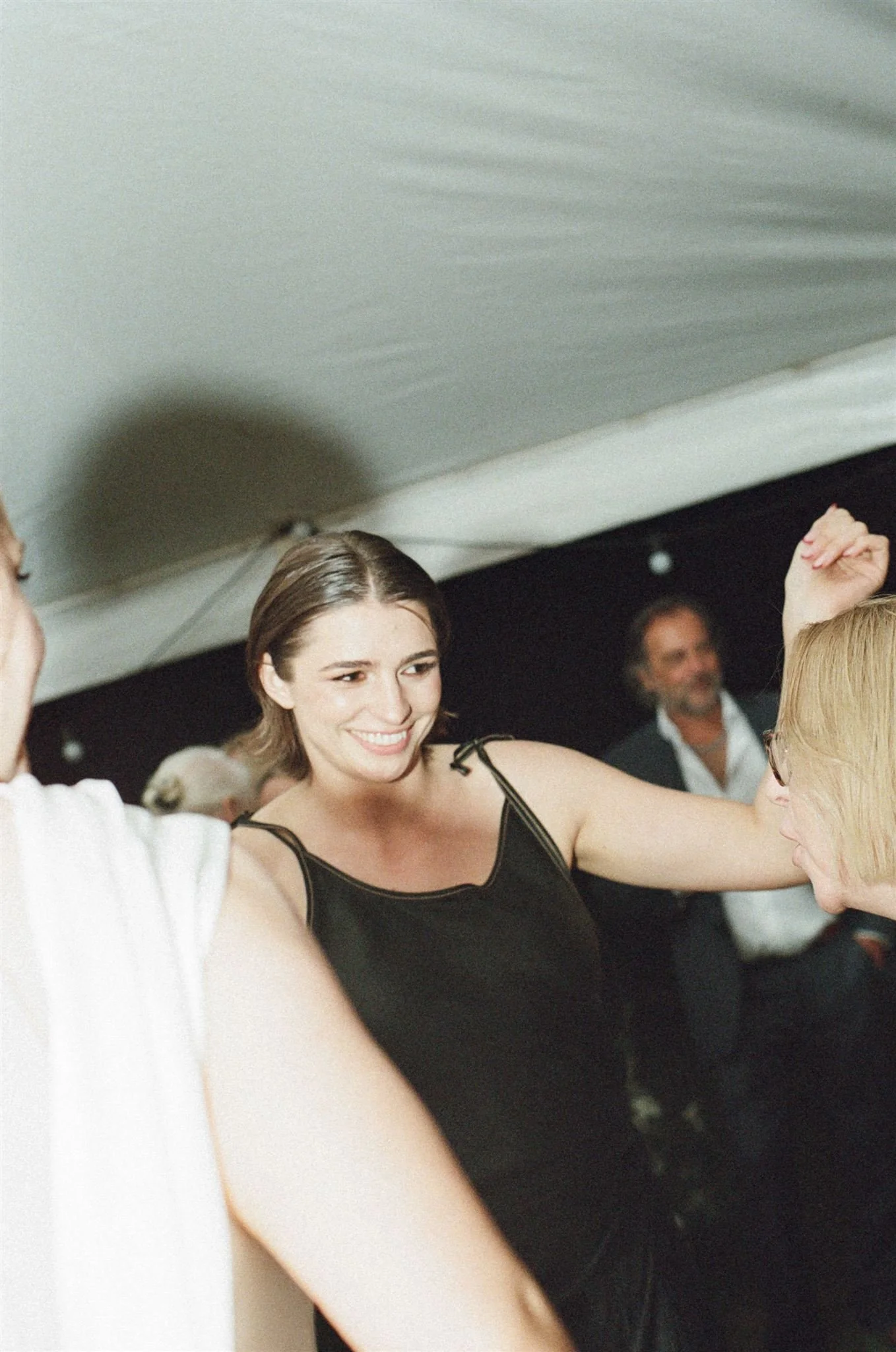 Wedding guest dancing in outdoor wedding tent, she is wearing a black dress.